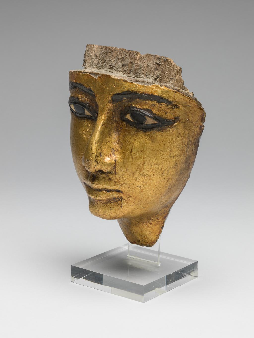 An image of Funerary Equipment/Coffin. Face from coffin, with eyes and eyebrows inlaid, gilded. Production Place/Find Spot: Egypt. Wood (gilded), carved, depth 7.5 cm, length 16.6 cm, width 11.9 cm, 1186-1069 B.C. Twentieth Dynasty, New Kingdom.