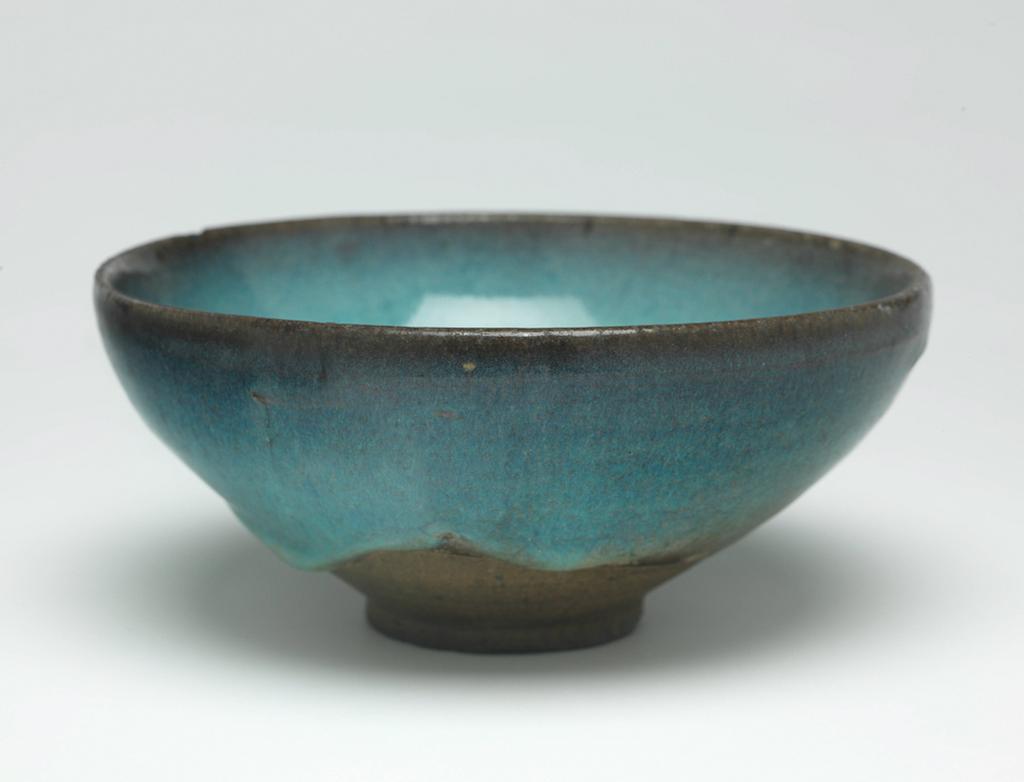 An image of Bowl. Jun ware. Circular with deep curved sides, standing on a footring. Oval label printed in black with a tower and 'Malcolm Collection', inscribed in blue black ink 'D./75'. Circular, inscribed in black '21'. Stoneware, covered in a pale blue glaze shading to purplish brown at the rim, and stopping short of the foot on the exterior. Height 7.4 cm, diameter 16.5 cm, 1000-1127. Northern Song (960-1127). Chinese. Acquisition Credit: Lent to the museum by Helen H. L. Whittow (nee Malcolm).