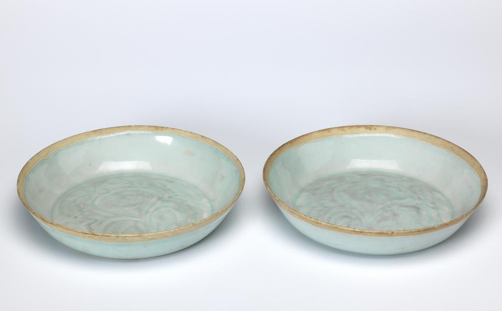 An image of Saucer dishes. Qingbai ware. A pair of porcelain saucer dishes. Acquisition Credit: Lent to the museum by Helen H. L. Whittow (nee Malcolm). ML.25A-1992:  With incised decoration under a pale greenish blue glaze, which covers the whole surface except for approximately 0.5cm on both sides of the rim. Circular with sloping sides and convex centre. The centre is incised with a formal plant motif. Oval label printed in black with a tower and 'Malcolm Collection' and inscribed in blue black ink 'D./34'. The base and the centre of the interior are worn, and there are several minute chips in the rim. Porcelain, incised and glazed, height 3.1 cm, diameter 15.2 cm, 1100-1279. Song Dynasty (960-1279). Chinese.ML.25B-1992:  With incised decoration under a pale greenish blue glaze, which covers the whole surface except for approximately 0.5cm on both sides of the rim. Circular with sloping sides and convex centre. The centre is incised with a formal plant motif. Oval label printed in black with a tower and 'Malcolm Collection' and inscribed in blue black ink 'D./35'. Slight wear to glaze on base, and in the centre where there is a small star shaped crack. orcelain, incised and glazed, height 3 cm, diameter 15 cm, 1100-1279. Song Dynasty (960-1279). Chinese.