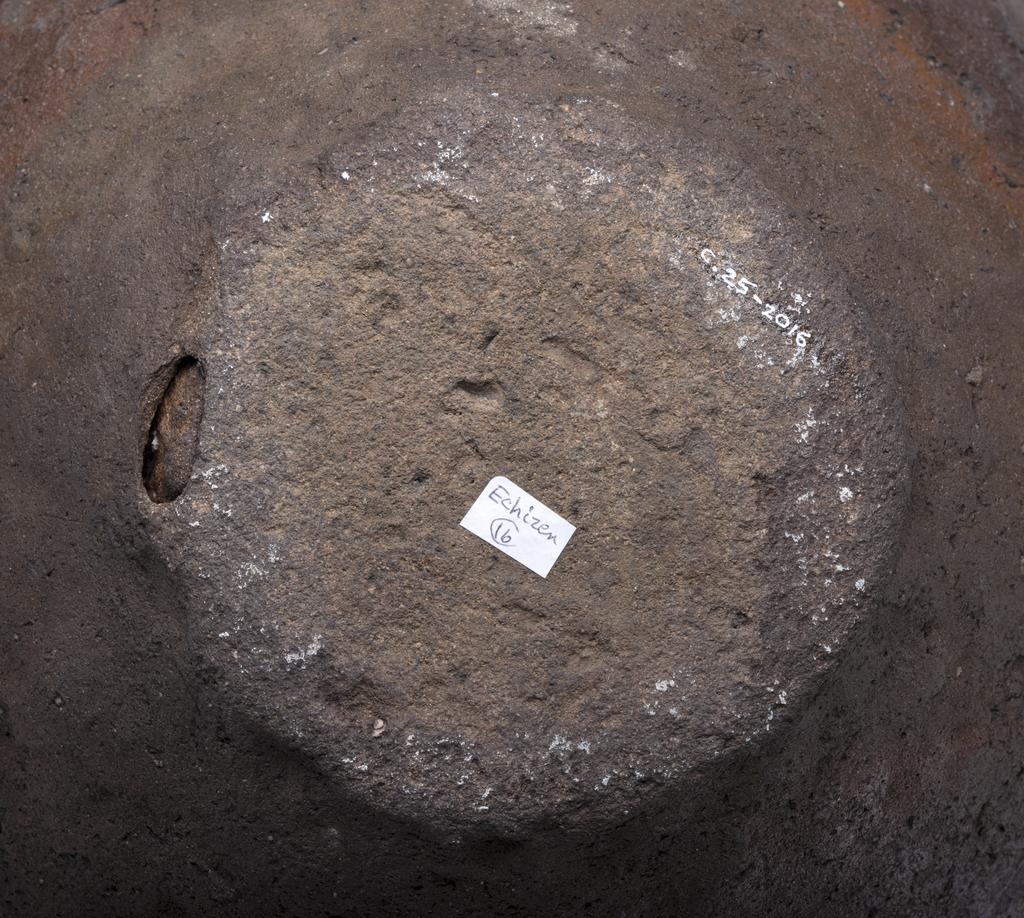An image of Studio Ceramics. Stoneware jar (tsubo). Oviform with a short neck and rounded rim. Characteristic dark red/brown body, with traces of fly ash glaze. With stone inclusions, one of which at the base forms a passage to the interior. No mark. 1500-1573. Japanese. Muromachi period (1336-1573). Acquisition: Dr John Shakeshaft Bequest.