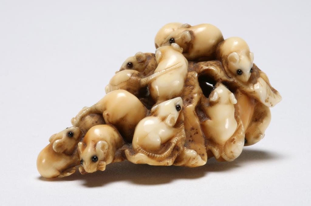 An image of Netsuke. Unknown maker, Japan. Carved with a group of rats chewing through a large radish. The eyes of rats are inlaid with horn. Ivory, carved, 1830-1870.