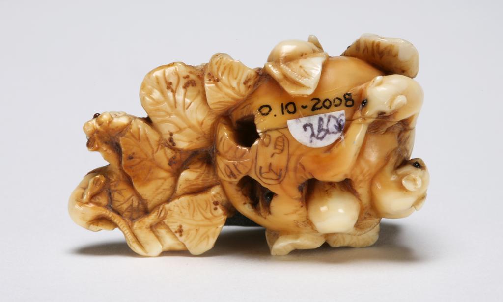 An image of Netsuke. Unknown maker, Japan. Carved with a group of rats chewing through a large radish. The eyes of rats are inlaid with horn. Ivory, carved, 1830-1870.
