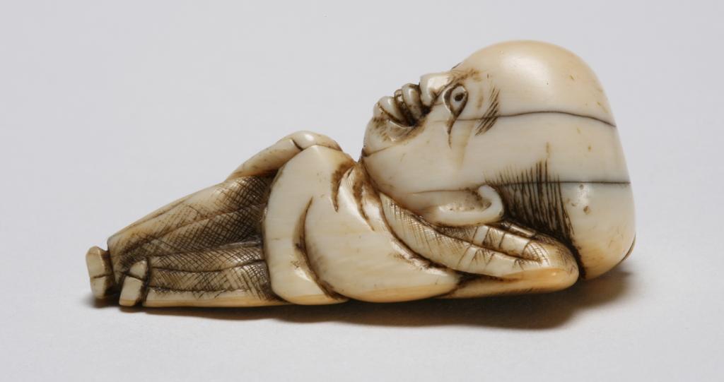 An image of Netsuke. Unknown maker, Japan. A Japanese big headed dwarf Fukusuke, making a face and sticking his tongue out. Ivory, carved, 1800-1840.