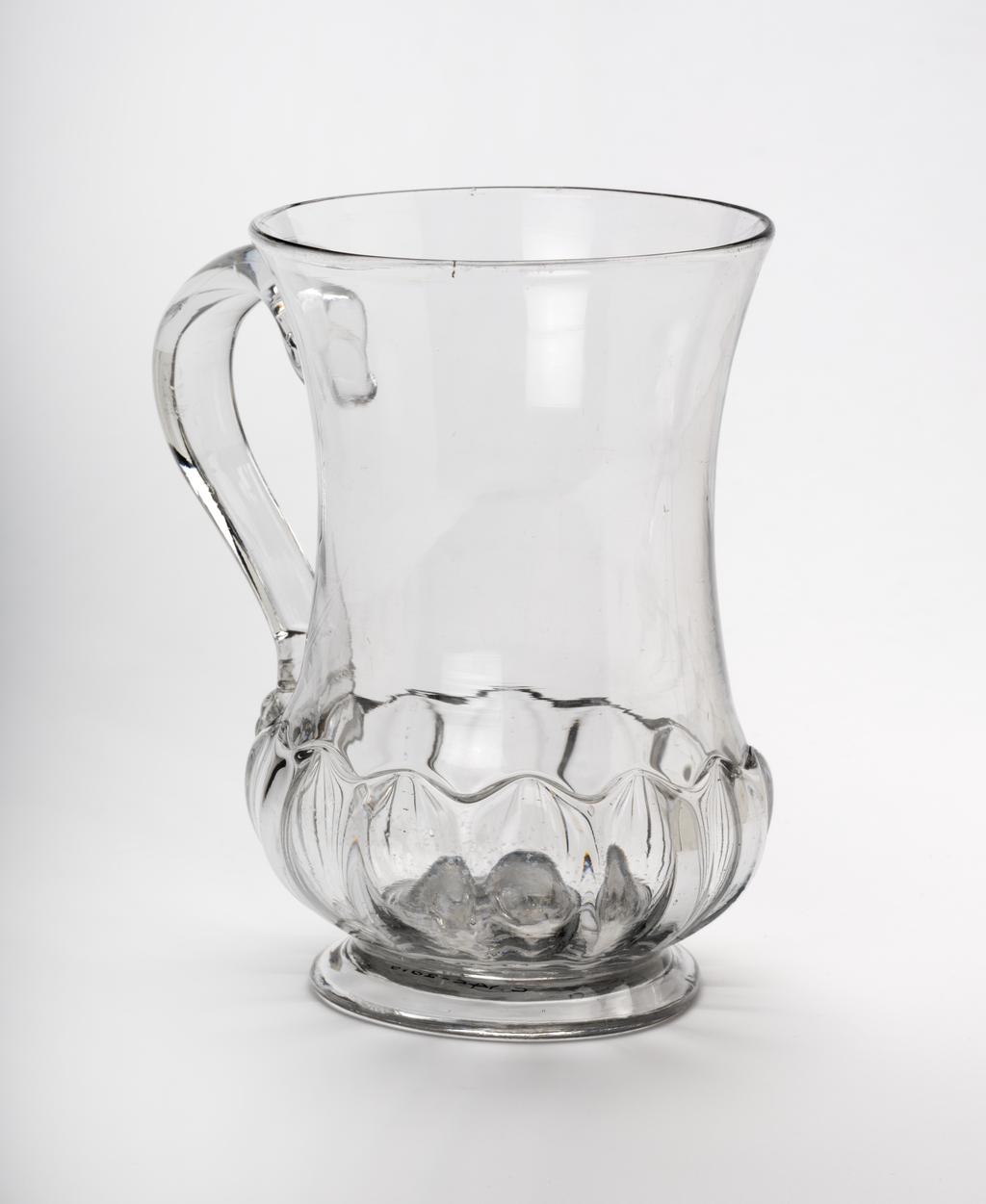An image of Mug. Tankard. Unidentified English glasshouse. The waisted thistle-shaped tankard has mould-blown gadrooning on its lower part, and stands on a low foot. The handle is of D-section and has a folded kick at the lower end. Clear lead-glass blown and mould-blown. 1720. Baroque. Sir Ivor and Lady Batchelor Bequest through The Art Fund.