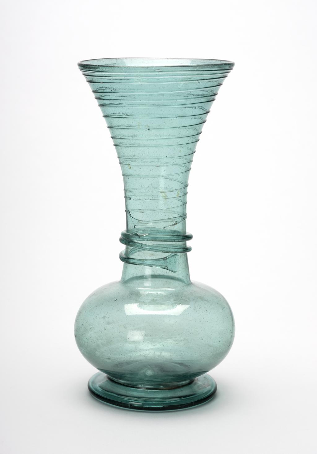 An image of Vase. Unknown glasshouse, probably Iran. The vase stands on a circular foot. The bulbous lower part rises into a cylindrical neck, which expands towards the open mouth. There is a pontil mark in the middle of the base. Transparent bluish-green glass, blown with applied thick and thin spirally-trailed threads round the neck, height, 20.3 cm, diameter, 9.8 cm, circa 1700-1750, probably 18th century. Production Note: Formerly attributed to Almeria in southern Spain, and dated to the 17th or 18th century. However, it seems more likely to have been made in Iran, probably 18th century, particularly as it came from a Iranian collection. Ivor and Lady Batchelor Bequest.