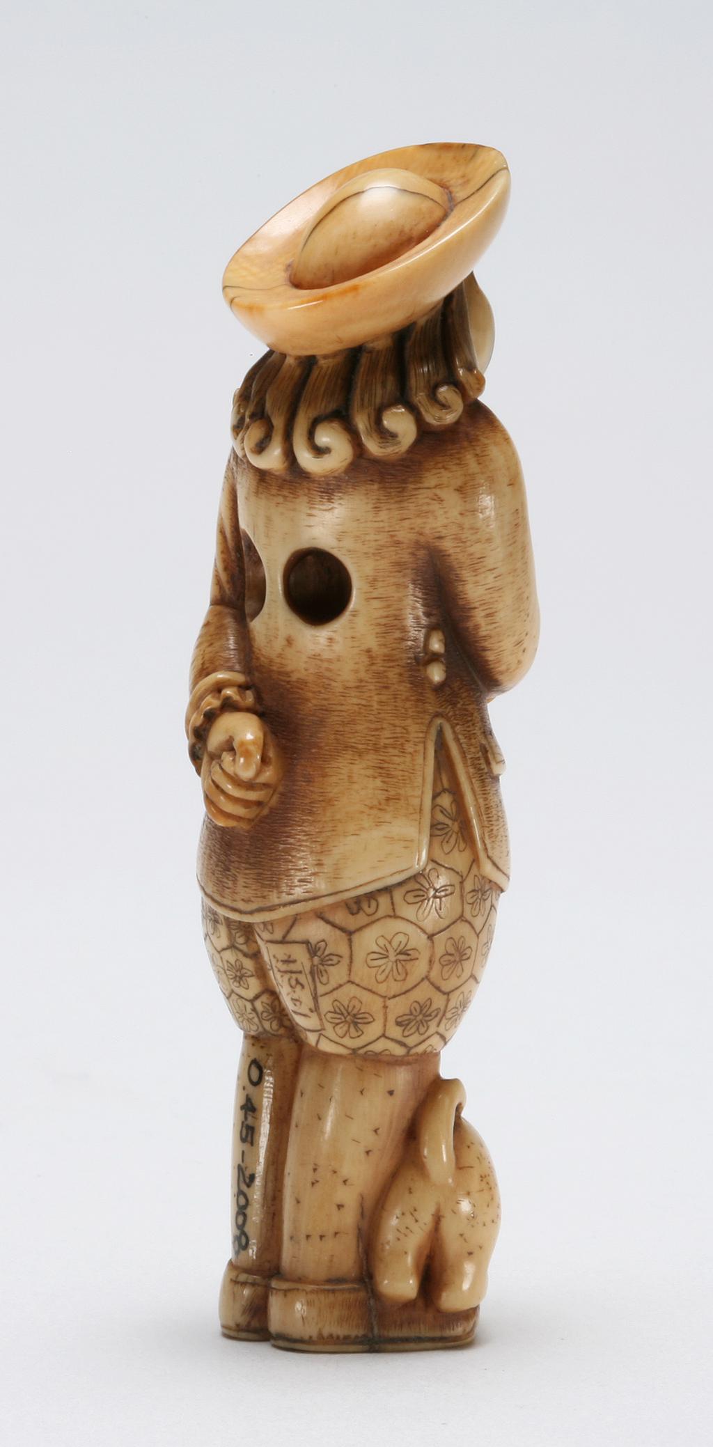 An image of Netsuke. Unknown maker, Japan. A Dutchman with wide brim hat standing, holding the leash of his pet dog. Ivory, carved, the dog’s eyes are inlaid with glass. Circa 1980.
