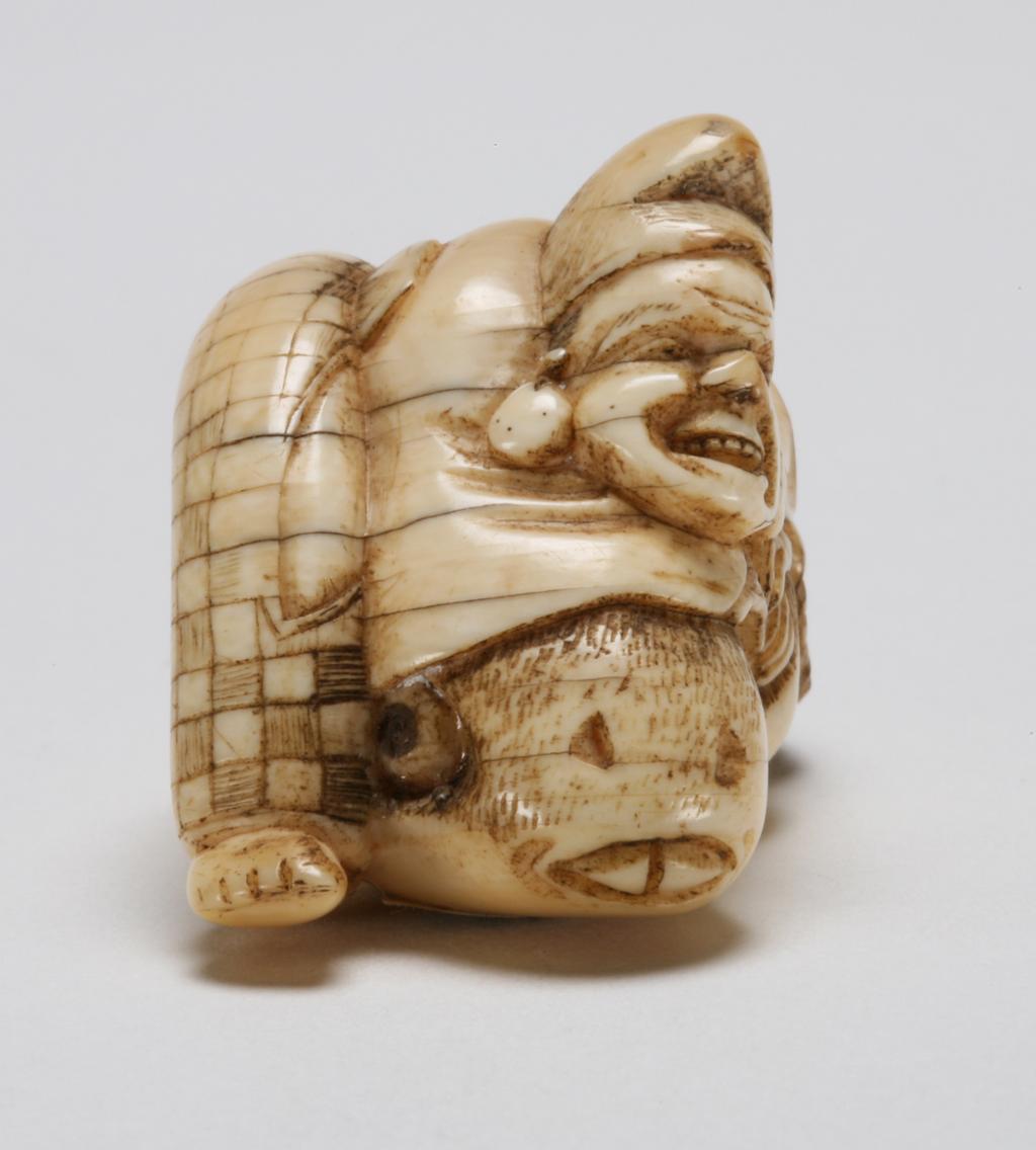 An image of Netsuke. Unknown maker, Japan. Ebisu is the protector of fisherman and merchants, he can be easily recognised by the court hat (Eboshi) and his fish. Here he tries to stop the large sea bream (Tai) moving away by leaning on top of the Tai. Ivory, the eyes of Tai-fish are inlaid with wood, 1800-1850.