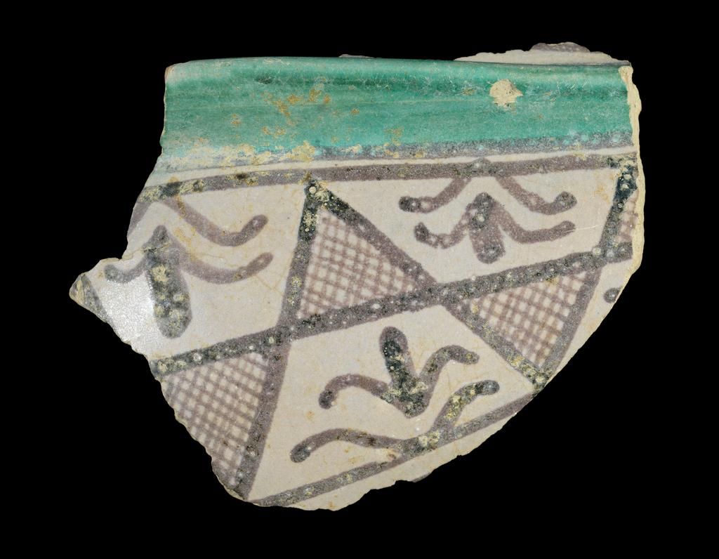 An image of Unknown. Maiolica. Fragment of a hollow vessel. Buff earthenware, tin-glazed greyish-white, painted in manganese and green, length 8.5cm, width 6.8cm, circa 1300-1400. Umbria, Italy.