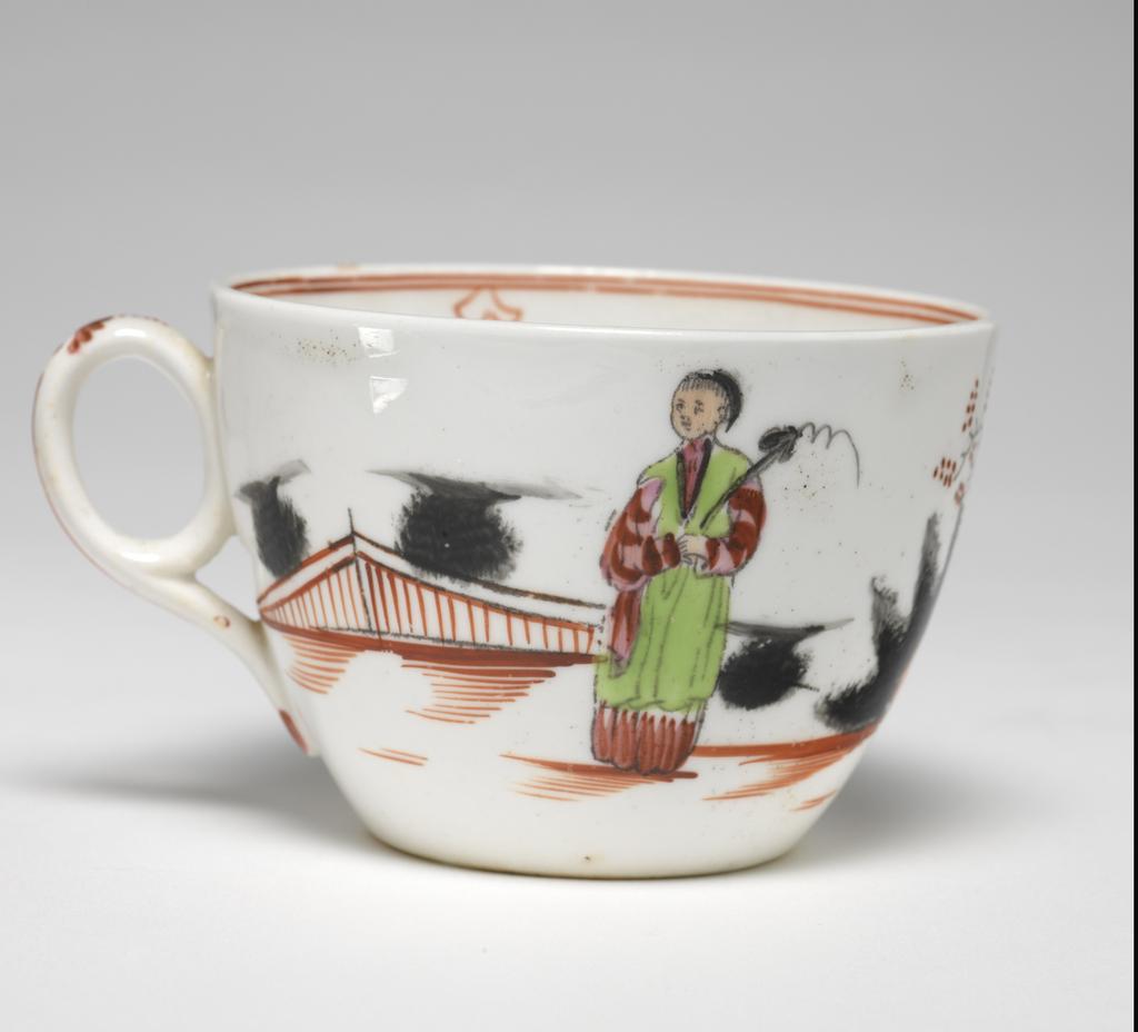 An image of Cup and saucer. New Hall Porcelain Factory, Staffordshire. Bute shape cup with oval ring handle. Circular saucer with curved sides, standing on a footring. The interior of the cup is decorated at the bottom with a row of red grasses, and round the rim with two narrow red lines under which are four inverted hearts with a circle below. The exterior is decorated with a continuous Chinese scene: two fuzzy black bushes behind a red fence; a woman wearing green and puce clothing, stands holding a sceptre; a spiky black bush and a flowering tree; a boy dressed in green and dark puce who is trying to catch a butterfly; two black bushes flanking a flowering tree; a standing man dressed in blue, and another black bush. The ground is indicated by horizontal red strokes. On the back of the handle in puce are five dots, a stylized leaf, a vertical stroke, and at the lower end two leaves. The saucer is decorated inside with a Chinese scene with spiky black rocks, a flowering shrub and flowering tree; a boy holding up arms to a butterfly, and a man and woman standing side by side, dressed similarly to those on the cup. The border is similar to that on the cup with six heart motifs. Pattern 421. Saucer of hard-paste porcelain, press-moulded, painted overglaze in enamels; cup is possibly bone china, lead-glazed, height, cup, 6 cm, width, cup, 10.5 cm, diameter, cup, 8.5 cm, height, saucer, 3 cm, diameter, saucer, 14.3 cm, circa 1800- 1805. Chinese Style.