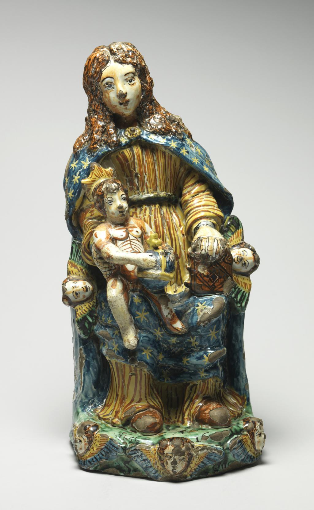 An image of Maiolica. Figure Group. The Virgin and Child enthroned. Unidentified Deruta potter, Umbria. The Virgin sits on a semi-circular throne with a winged cherub's head on each side at the front. She wears a long-sleeved yellow and orange striped gown and a blue cloak scattered with yellow stars. The infant Christ holding an orb sits on her right knee, and she supports a book on her left knee. The green base is decorated along the shaped front edge with three winged cherub's heads in relief. The top is inscribed in manganese `CF/PC/1676 16../S M'. The back of the throne is inscribed in blue `A.D.22D./MARZO/ 1676/.CDF./ P '. Dark buff earthenware, moulded and modelled in the round; tin-glazed on the exterior and on the hollow interior. Painted in dark blue, green, yellow, brownish-orange, and manganese-purple. Height, whole, 38.5 cm, width, base, 18.4 cm, depth, base, 24.0 cm, dated 22 March 1676. Baroque.