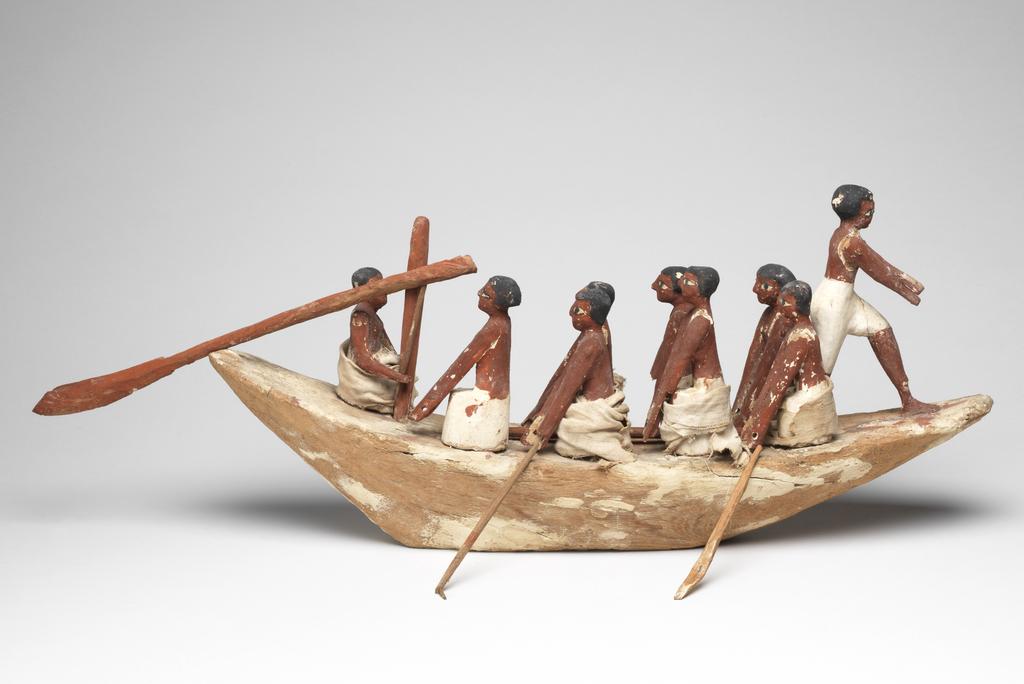 An image of Model Boat. Wooden model of a rowing boat with seven oarsmen (one missing at the front); a look-out on the prow; and a stroke caller (cox) in the bow. He sits beside a rudder-oar. The figures have white painted kilts and red-brown flesh. Some figures have real linen loin cloths. Production Place: Egypt. Find Spot: Tomb of Khety, tomb 366 (Beni Hasan), Egypt. Painted wood, linen, height, 25 cm, length 59 cm, width 12 cm, circa 2010-circa 1950 B.C. 12th Dynasty, Middle Kingdom.