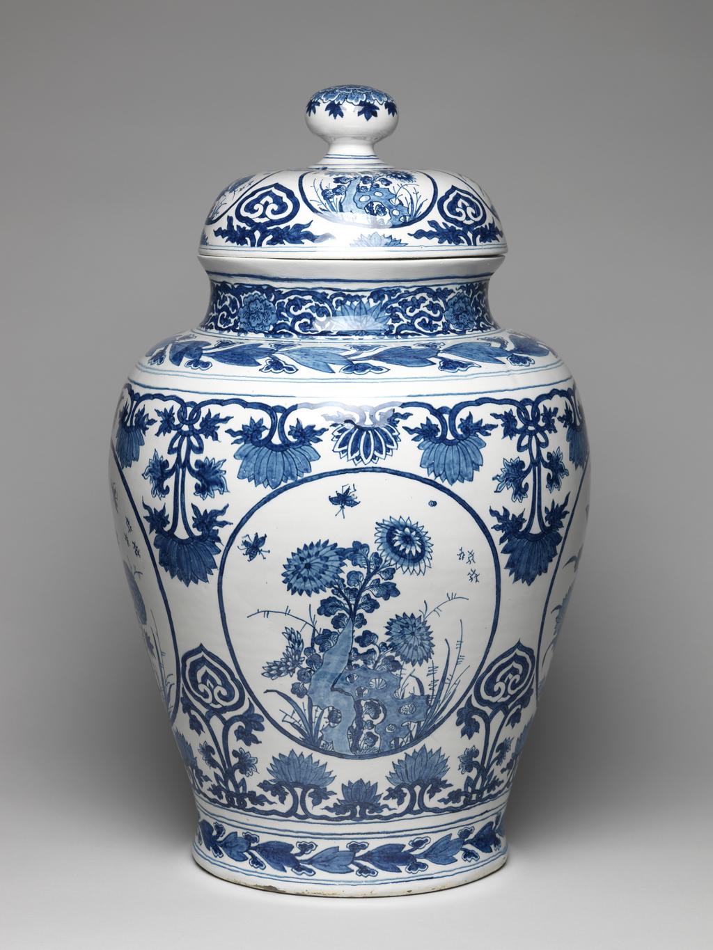 An image of Delftware. Covered vase. Drie Posteleyne Astonne factory, Holland, Delft. Kamm, Gerrit Pietersz, proprietor of pottery. Painted in blue in Oriental, Chinese, style. The oviform vase has a short concave neck, and a domed cover with a rounded knob. On both the vase and cover there are four oval panels containing Chinese peonies, chrysanthemums and lotus-plants, separated by lotus-scroll ornament and cloud-scrolls. Round the shoulder and round the base of the vase there are horizontal borders of stylized foliage between narrow bands. The neck is decorated with lotus and scrolls between narrow bands. The knob is decorated with a multi-petalled flower. Pale buff earthenware, thrown, tin-glazed, and painted in cobalt blue, height, whole, 60.5 cm, height, vase, 47.2 cm, width, base, 24.5 cm, circa 1685-1700. Production Note: The mark indicates that the vase was made at Die Posteleyne Astonne factory during the proprietorship of Gerrit Pietersz Kamm from 1679-1700.