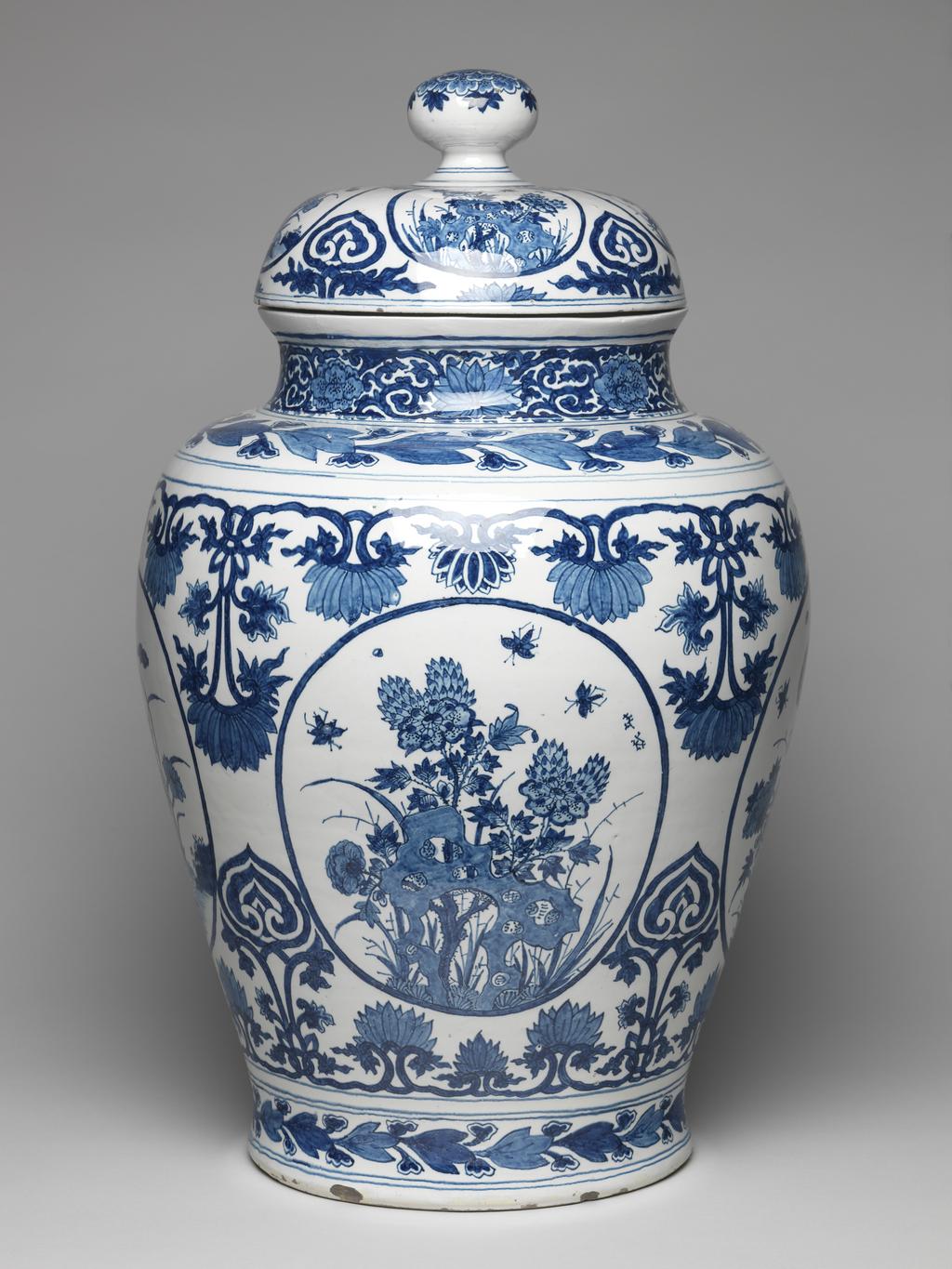 An image of Delftware. Covered vase. Drie Posteleyne Astonne factory, Holland, Delft. Kamm, Gerrit Pietersz, proprietor of pottery. Painted in blue in Oriental, Chinese, style. The oviform vase has a short concave neck, and a domed cover with a rounded knob. On both the vase and cover there are four oval panels containing Chinese peonies, chrysanthemums and lotus-plants, separated by lotus-scroll ornament and cloud-scrolls. Round the shoulder and round the base of the vase there are horizontal borders of stylized foliage between narrow bands. The neck is decorated with lotus and scrolls between narrow bands. The knob is decorated with a multi-petalled flower. Pale buff earthenware, thrown, tin-glazed, and painted in cobalt blue, height, whole, 60.5 cm, height, vase, 47.2 cm, width, base, 24.5 cm, circa 1685-1700. Production Note: The mark indicates that the vase was made at Die Posteleyne Astonne factory during the proprietorship of Gerrit Pietersz Kamm from 1679-1700.