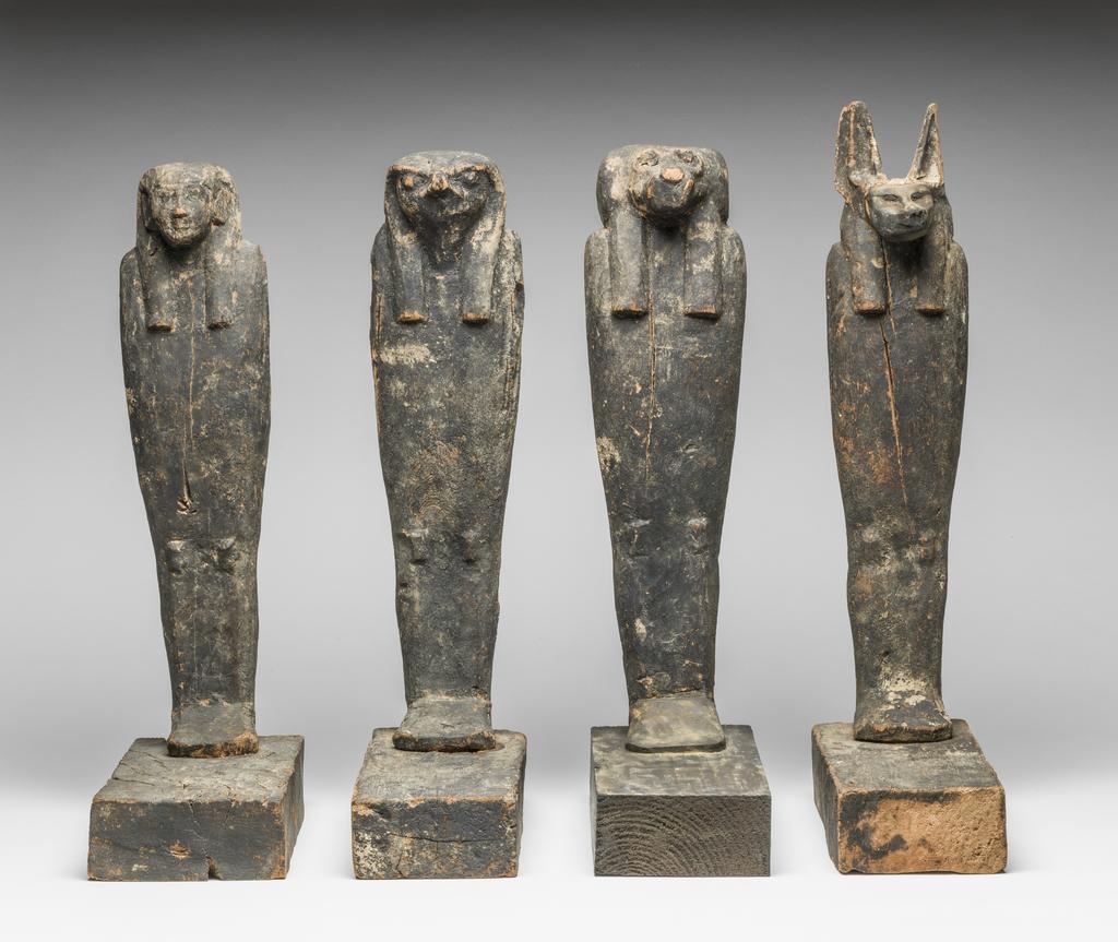 An image of Figure. Son of Horus, human headed mummiform figure, standing on rectangular base, black resin coating, buried with Nakhtefmut. Production Place: Egypt. Find Spot: Ramesseum, Thebes, Egypt. Wood, depth 21.5 cm, height 37.5 cm, width 10.2 cm, circa 923 B.C. Twenty-second Dynasty; Third Intermediate period.