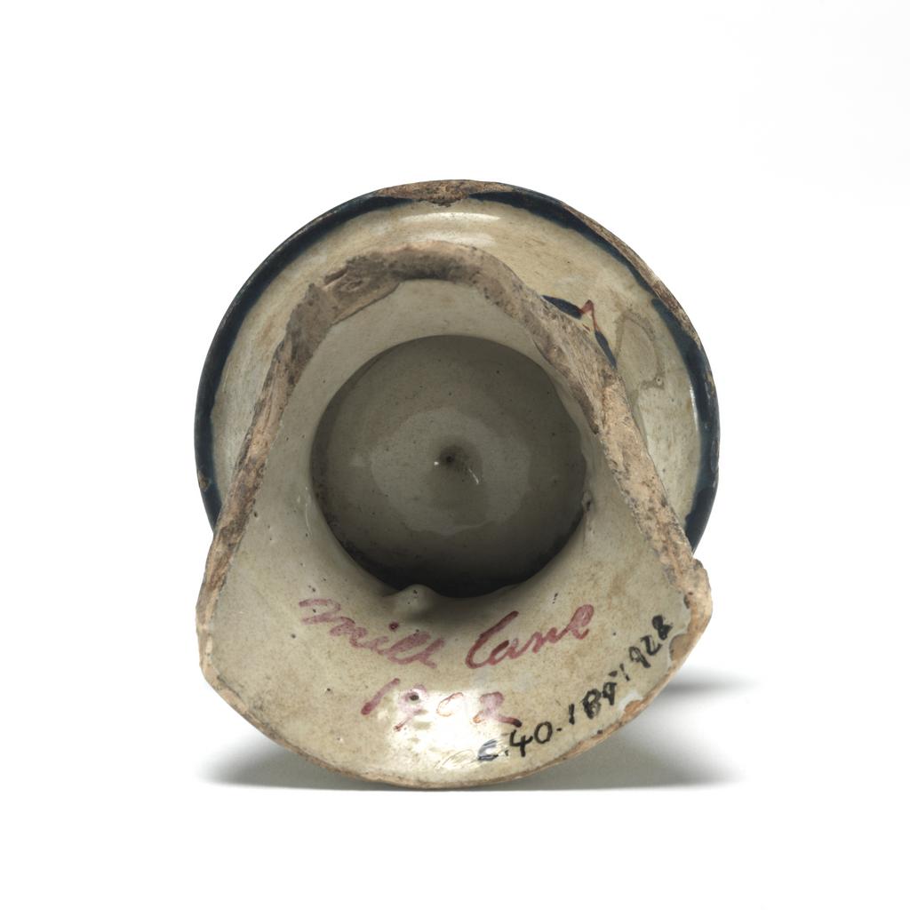 An image of English Delftware. Salt. Part of a salt. Uncertain factory, London, Vauxhall, or Bristol. Of capstan form with an outward curving rim, and a shallow bowl-shaped depression for the salt in the top. About two-thirds of the lower part is missing. The sides are decorated in all three colours with stylized flower and leaf motifs with detached blue flower heads and paired leaves between them. There are two blue bands round the lower edge, and on the rim, a border of semi-circular petals striped in red reserved in a blue ground. The middle of the salt pan is decorated wtih a pair of leaves within two concentric blue circles. Buff earthenware tin-glazed, painted in blue, red, and green, height 5 cm, width, rim 7 cm, circa 1720-1730. English.