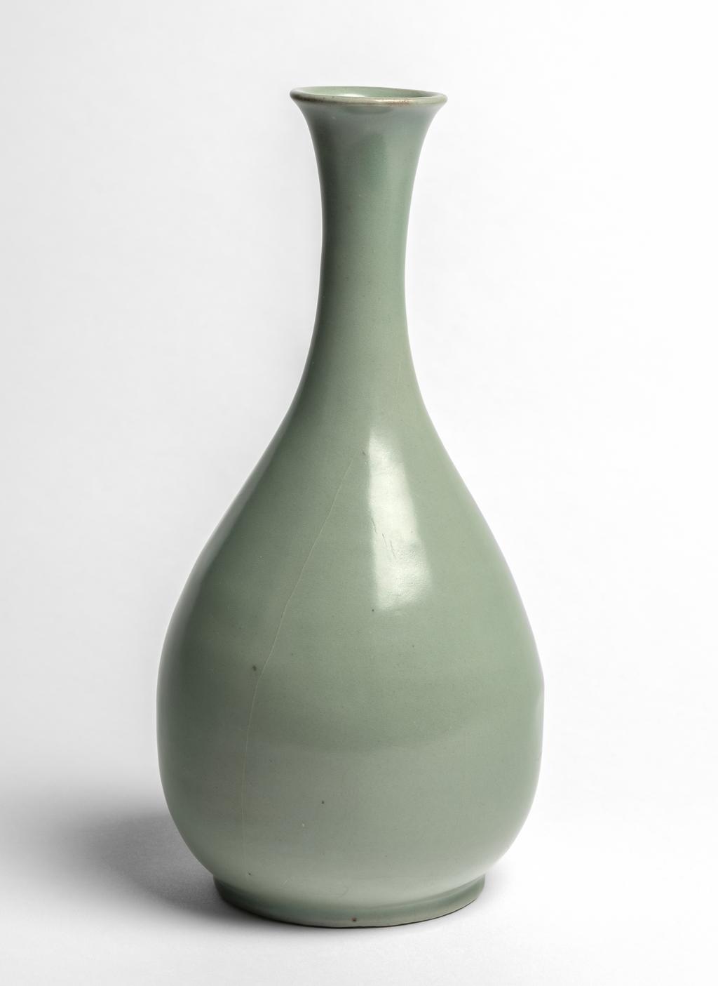 An image of Wine bottle. Unknown pottery, Korea, South Cholla province, Kangjin-gun, Sadang-ri kilns. This bottle has an elegant outline, with a long neck that flares towards the mouth, and a pear-shaped body. It is completely plain. The foot is wide but very low. The body is of fine clay; the clear semi-transparent glaze is evenly applied all over the body and subtly shimmers in a fine jade colour. The foot is completely glazed, and the base shows five quartzite spur-marks. Stoneware, thrown and celadon-glazed. Height, bottle, 29.6 cm, diameter, rim, 5.4 cm, diameter, foot, 9.8 cm, circa 1100-1150. Koryo Dynasty.