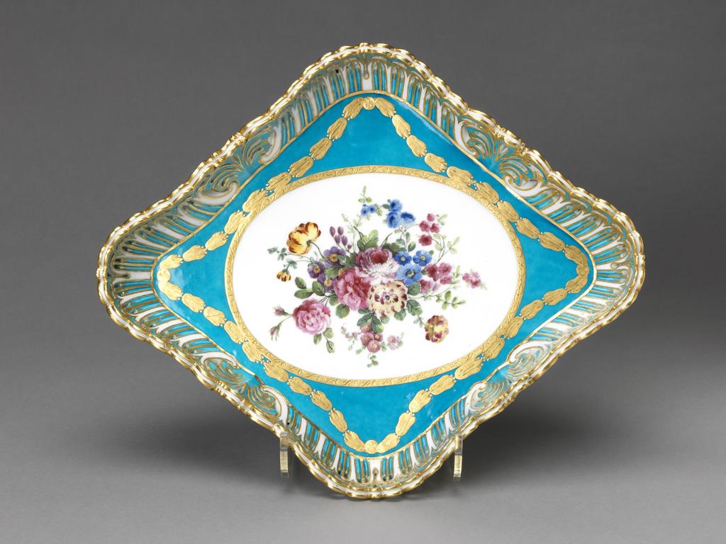 An image of Tray/Plateau losange corbeille à jour. Sèvres Porcelain Manufactory. Censier, Charles, répareur, possibly (French, op. 1758-1775). Soft-paste porcelain with pierced sides, decorated with a bleu céleste ground, a reserve painted in enamels with a bouquet of flowers, and gilding. height 5.5 cm, length 30.5 cm, width 25.5 cm, 1769. Rococo. Louis XV.