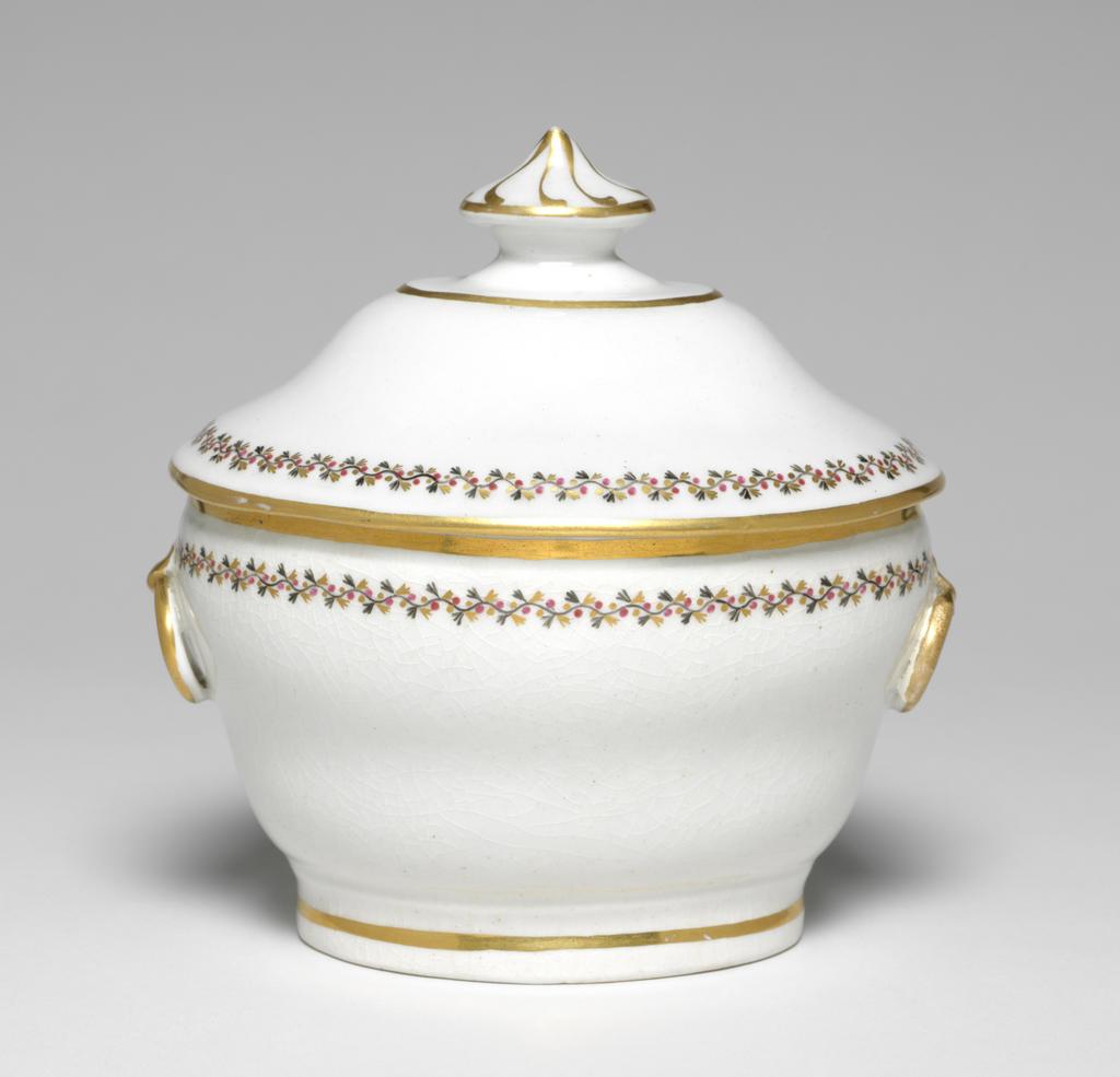 An image of Sugar Bowl/Sugar Basin. New Hall Porcelain Factory, Staffordshire. Of oval, ogee form with an applied ring handle at each end, standing on a footring. The cover is of slightly ogee form with a small oval platform and an oval pointed knob on top.The exterior of the bowl is decorated with a border comprising a black wavy stem with small trefoil leaves, puce berries, and gold trefoil leaves. The handles are gilded and there are gold bands just below the rim, and round the footring. The cover is decorated with a similar border, and with gold bands round the edge, the edge of the platform and the knob, which also has eight swirling gold lines radiating from the point. Pattern no. 280. Hybrid hard-paste porcelain, moulded, with crazed glaze, painted overglaze in black and puce enamel, and gilded. Height, whole, 14.7 cm, length, whole, 14.5 cm, width, whole, 10.5 cm, circa 1797-1803.