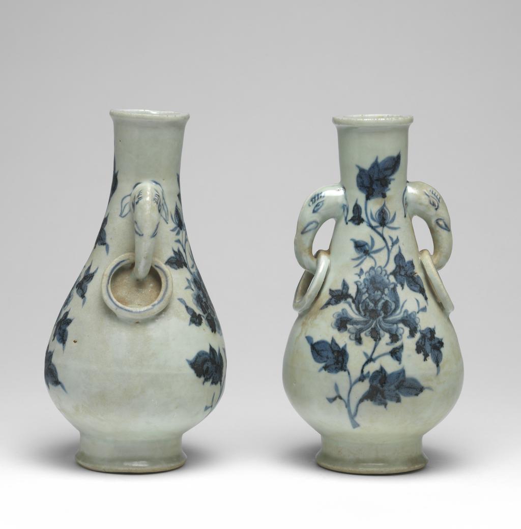 An image of Vase with elephant handles. Unknown maker, China, Folk kilns. The pear-shaped vase has a slender neck, thick, rounded lip, and two elephant head and fixed-ring handles. The body tapers to a deep, flared foot with deep flat, recessed base. The elephant handles are finely painted with eyes, eyelashes, tusks and ears, and the fixed rings with single circle ornament. On each side of the body are elegant peony sprays in blue. The interior is unglazed, as is the base which is covered with a red, sandy deposit. Hard-paste porcelain, thrown, painted in underglaze blue, with base and interior unglazed. Height, whole, 24.6 cm, diameter, whole, 12.7 cm, circa 1300-1368. Yuan Dynasty (1206-1368). Collection: H.S. Reitlinger. Of a pair of vases, with C.689B-1991.