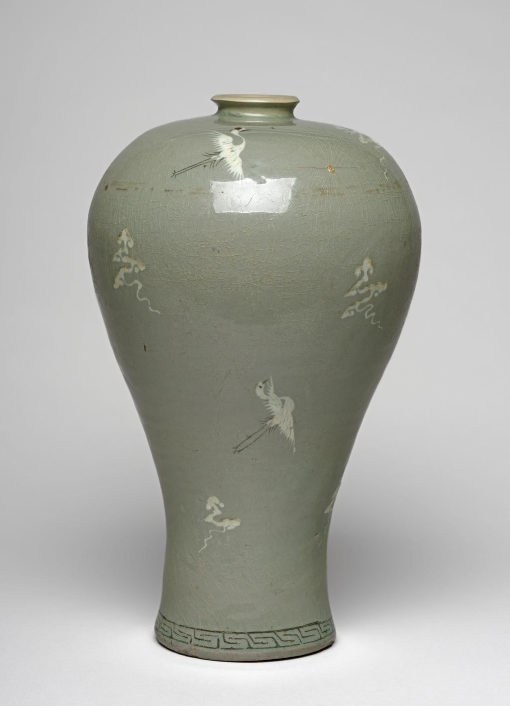 An image of Maebyong. Vase with cranes and clouds. Unknown pottery, Korea, North Cholla province. Yuch'on-ri, Puan. This maebyong-shaped vase has a wide almost flat shoulder and a full body that gradually tapers towards the spreading foot. The foot-rim is broad and shallow. The everted mouth is restored and does not correspond to the original form, which would have been of angled cup shape. A band of key-fret is inlaid in black slip around the base. Cranes and cloud motifs are sparsely arranged over the whole vessel with a lot of breathing space between; they are inlaid in black and white slip and emphasised with touches of underglaze copper-red, adding accents of brighter colour. The glaze is thinly but unevenly applied; it is glossy and has a pale blue-green tone. The whole surface is covered with a fine crackle. The foot shows traces of fire-clay spurs. Stoneware, thrown, inlaid in black and white slip, with details painted in copper-red, and celadon-glazed. Height, whole, 30.6 cm, diameter, rim, 4.8 cm, diameter, foot, 10.0 cm, circa 1150-1200. Koryo Dynasty. Notes: Vessels such as this one were used for wine.