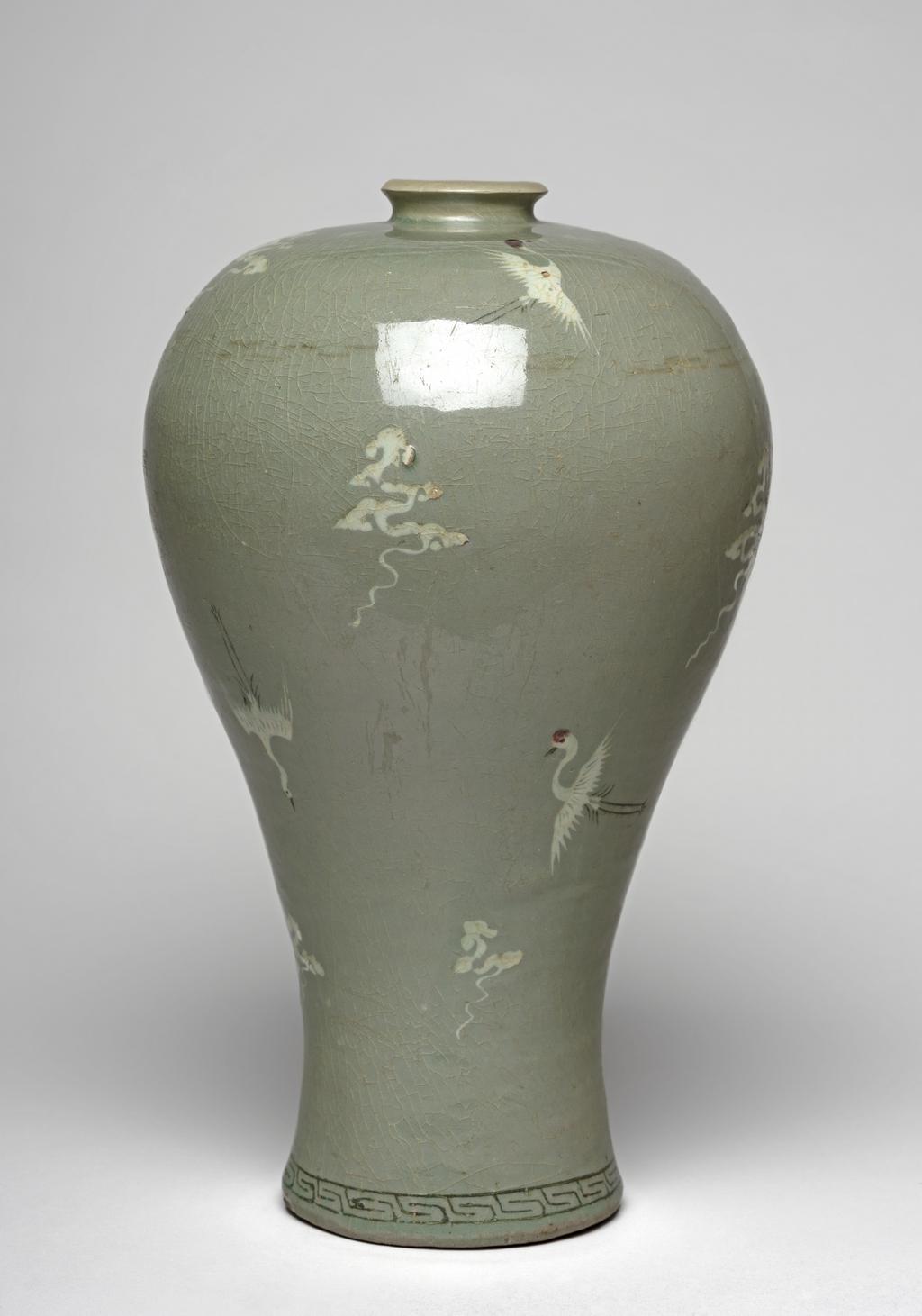 An image of Maebyong. Vase with cranes and clouds. Unknown pottery, Korea, North Cholla province. Yuch'on-ri, Puan. This maebyong-shaped vase has a wide almost flat shoulder and a full body that gradually tapers towards the spreading foot. The foot-rim is broad and shallow. The everted mouth is restored and does not correspond to the original form, which would have been of angled cup shape. A band of key-fret is inlaid in black slip around the base. Cranes and cloud motifs are sparsely arranged over the whole vessel with a lot of breathing space between; they are inlaid in black and white slip and emphasised with touches of underglaze copper-red, adding accents of brighter colour. The glaze is thinly but unevenly applied; it is glossy and has a pale blue-green tone. The whole surface is covered with a fine crackle. The foot shows traces of fire-clay spurs. Stoneware, thrown, inlaid in black and white slip, with details painted in copper-red, and celadon-glazed. Height, whole, 30.6 cm, diameter, rim, 4.8 cm, diameter, foot, 10.0 cm, circa 1150-1200. Koryo Dynasty. Notes: Vessels such as this one were used for wine.