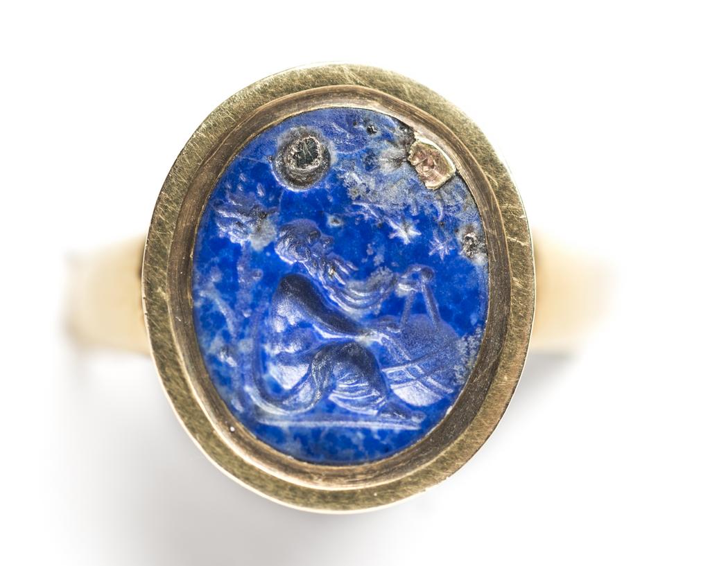 An image of Engraved gems/ringstone/intaglio. An astronomer wearing a himation, left arm and shoulder bare, sitting on the ground beneath a tree, in profile to the left. He is measuring a globe with compasses held in his right hand; the sun, the moon and five stars above him, formerly picked out with pyretic inclusions. Mount: gold ring, type 1a. Intaglio cutting. Lapis lazuli, 12.5 mm, 10.5 mm, circa 1500-1600.