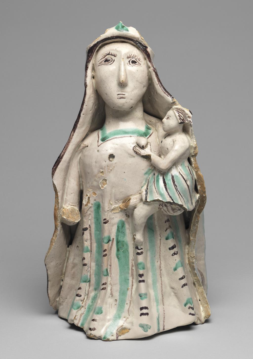 An image of Maiolica arcaica figure group. Standing Virgin and Child. Unidentified Orvieto pottery, Umbria. The Virgin stands holding the infant Christ in her left arm. Christ wears a skirt, and she wears a long pleated gown and a cloak over her head which falls down over her shoulders to the ground. The Virgin's costume is decorated with vertical rows of slanting manganese and green strokes between wide green and narrow manganese stripes. Christ's skirt has close-set stripes of alternate colours. The figure of the Virgin is hollow and the head was made separately and set into the body before firing. Greyish-buff earthenware, tin-glazed greyish-white on the exterior, and painted in manganese and copper-green, height, whole, 32.0 cm, depth, front-back, 18.0 cm, circa 1350-1450.