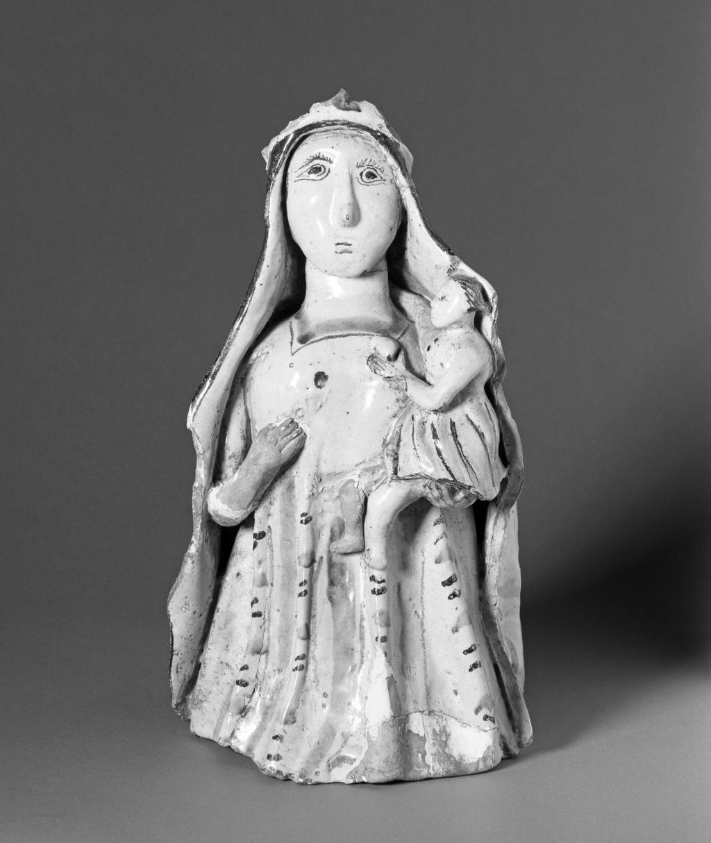 An image of Maiolica arcaica figure group. Standing Virgin and Child. Unidentified Orvieto pottery, Umbria. The Virgin stands holding the infant Christ in her left arm. Christ wears a skirt, and she wears a long pleated gown and a cloak over her head which falls down over her shoulders to the ground. The Virgin's costume is decorated with vertical rows of slanting manganese and green strokes between wide green and narrow manganese stripes. Christ's skirt has close-set stripes of alternate colours. The figure of the Virgin is hollow and the head was made separately and set into the body before firing. Greyish-buff earthenware, tin-glazed greyish-white on the exterior, and painted in manganese and copper-green, height, whole, 32.0 cm, depth, front-back, 18.0 cm, circa 1350-1450.