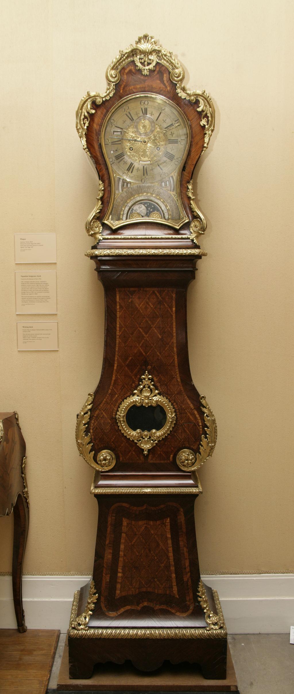 An image of Equation Longcase Clock. De Rabours, France, Paris, Colmar. Equation longcase clock with 8 day hour striking movement and perpetual calendar which takes account of leap year. Louis XV style case. Dial: Elaborately shaped dial plate 11 1/2 inches wide and 17 inches high, with applied English style chapter ring and seconds ring. The dial plate gilt, the chapter ring and all subsidiary dials silvered. Signed on lower edge of chapter ring ‘De Rabours A Paris' and at base of dial plate ‘Perfectione par Meunier horloger Paris an.1782'. The lower third of the dial is occupied by a semi-circular day of the month indicator with fly back hand, and within the date ring is a simple lunar dial with a scale of days 1 - 29 1/2 and a rotating disc with two moons to point to the age alternately and show the phases. Below the chapter ring at VII are openings to show the times of sunrise and the sun's position in the zodiac. Similar openings below V show the times of sunset and an annual calendar. A slot inside the chapter ring above VI shows the year in the leap year cycle. The day of the week is shown in a slot in the chapter ring near X. The calendar is set by means of a small squared arbor in an aperture in the chapter ring between VIII and IX, with an adjacent opening so that the calendar can be set to change over at midnight. A lever in a slot outside the chapter ring at X is used to set the maintain¬ing power. Mean time is indicated by pierced and carved gilt brass minute and hour hands, and solar time is shown by a blued steel minute hand. The brass seconds hand is a replacement of 19th century English type. Movement: 8 day hour striking movement with equation of time and perpetual calendar which takes account of leap year. The going train is weight driven with an anchor escapement and bolt type main¬taining power without shutters. The striking train is spring driven with a going barrel and strikes on the solar hours, which is usual on French equation clocks. The bell