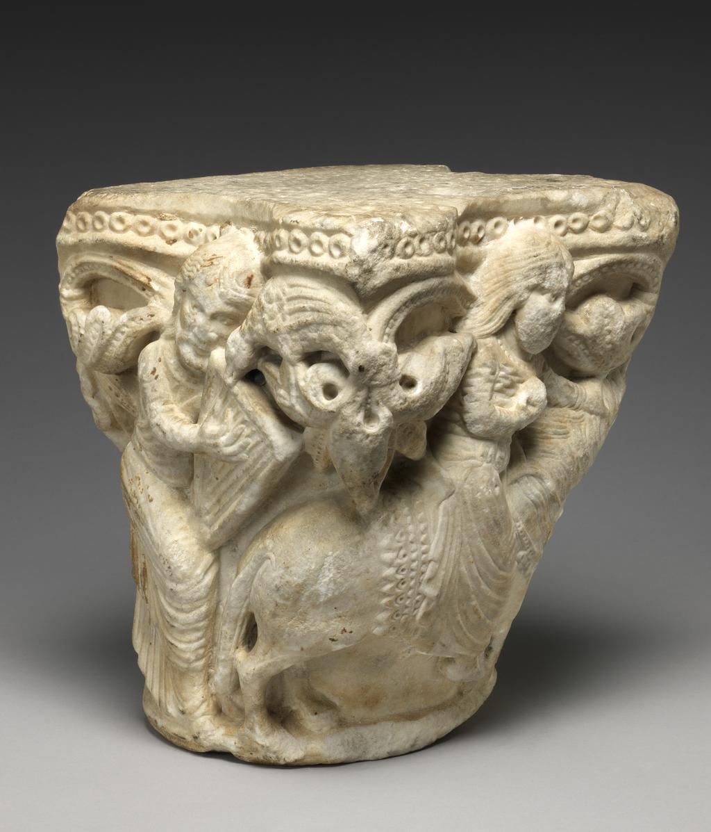 An image of Sculpture. Capital of a column, the sides carved with a man seated on a throne playing the harp, probably the psalmist, David, with an eagle above and to the right of him, a woman riding a horse, possibly the Virgin Mary, and another woman leading the horse with her right hand and holding an eagle on her left. Round the upper edge there is a row of drilled beading with below, foliated scrolls flanking the figures. White marble, carved and drilled, height, whole, 29.8 cm.  Production Place: France, Avignon. Probably from the Romanesque cloister of Notre-Dame-des-Doms, Avignon. Circa 1150-1200. Romanesque.