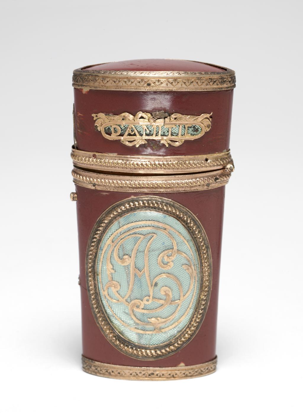 An image of Etui. Objet de vertu/nécessaire. Spaendonck, Gerard van (Dutch, 1746-1822). Unknown box maker, France. With an oval miniature of a carved stone urn of flowers and a nest. The tapering flattened cylindrical etui necessaire has a slightly domed hinged lid with a catch, which is released by a button on the right hand side with a thumb plate above. The mounts round the miniature, initial and rims are embossed with ropework, those at the top and bottom of the etui are engraved with a pattern of zig-zags and scrolls. The front and back of the lid each have an openwork gold plaque pinned over pale green metallic foil, bearing the words 'NECESAIR' and 'D’AMITIE' respectively, framed by ribbons. On the front is a miniature, possibly painted on card. On the back is an elaborate gold openwork initial 'A' on a green metallic foil ground, under glass. The miniature depicts a two-handled stone vase carved with a cherub, containing flowers including roses, hyacinth, forget-me-nots, auricula and morning glory, next to a nest of leaves containing three eggs, all on a marble slab against a dark grey ground. The etui contains a pair of scissors, an ivory tablet with a gold stud, a pencil, a bodkin and another implement in separate compartments lined with red velvet. Red lacquer, probably on ivory, with gold mounts, a miniature on the front face and an initial on the back. Height, whole, 2.1 cm, length, whole, 8.0 cm, width, whole, 5.0 cm, circa 1766 to before 1822. Collection: Major, the Hon. H.R. Broughton.
