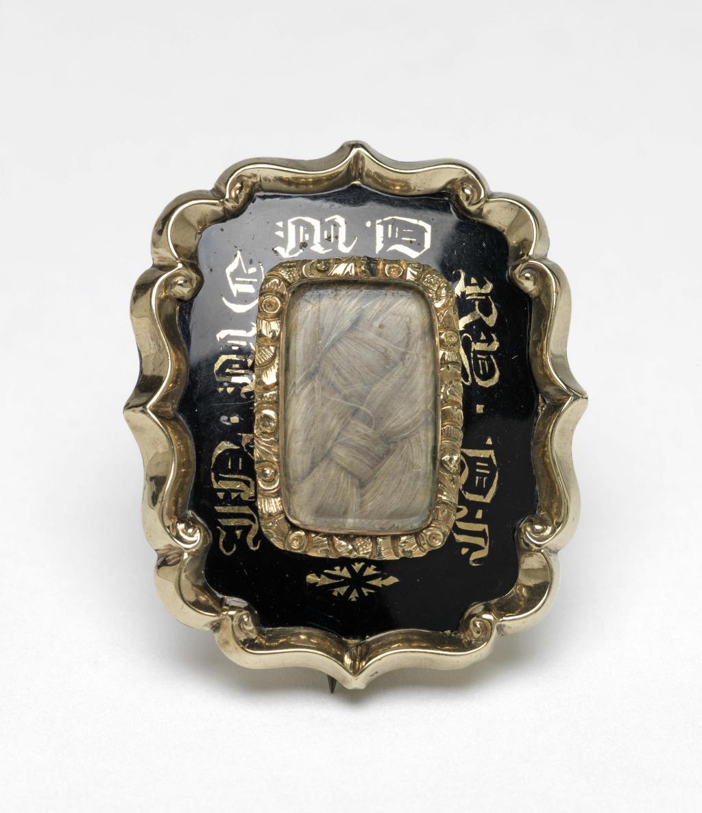 An image of Jewellery. Mourning brooch. Unknown maker, probably Ireland or England. Rectangular brooch, with a gold outer frame that has round corners and raised cusped and scalloped edges, with, in the centre, a rectangular compartment containing inter-woven blonde hair under glass, mounted in a plain gold rub-over setting, surrounded by a foliated gold frame. Between the outer and inner frames, the flat area of the brooch is enamelled onto a copper alloy plate in a translucent dark blue enamel that optically appears opaque black, and bears a gilt flower head at one end, the gothic initials MD at the opposite end, and, on the two long sides, the gothic initials RD, DI? and J?N?, MT? respectively. The gold back-plate is engraved 'Matilda/Obit 17th Feby/1842'. Brooch-pin fastening on the back: silver alloy or nickel-silver catch-plate and hinge-plate with a copper alloy (probably copper) pin. The lower quality of the fastening and excess solder around the hinge-plate suggest the pin is a replacement or later addition. The hinge plate partly covers an indentation in the gold back-plate that may relate to an earlier fitting. Gold ring with black enamel decorated with gilding, containing plaited hair under glass, width, whole, 2.6 cm, length, whole, 3.2 cm, circa 1842. Notes: The brooch belonged to Matilda Barnes (1829-1914), née Armstrong, who was born and brought up in Ireland but lived in England after her marriage to the donor's late husband's grandfather. The inscription does not refer to a member of the family.