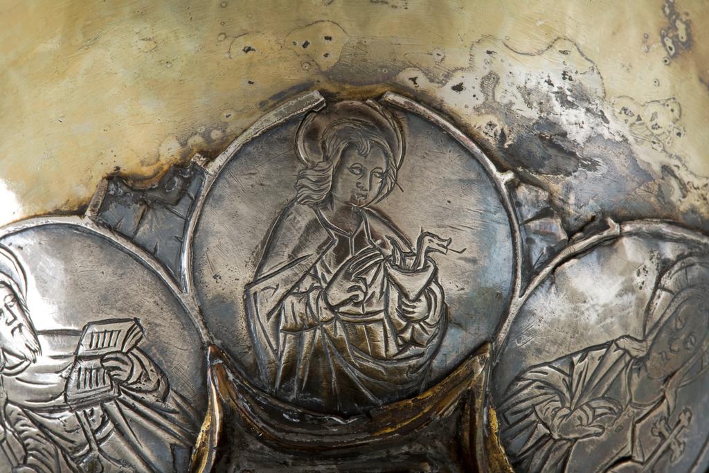 An image of Silver/Church Plate. Chalice. Petruccio Campagnini, Andrea, probably (active Tuscany, Siena, Italy). Set with six silver medallions of Christ, St Peter, St. Paul, St. John, St. Bartholomew and possibly St. Barnabus. Above the knop the stem is engraved with six male busts without nimbi; below the knop the stem is engraved with six birds. At the base of the stem are moulded borders containing a plain band engraved and enamelled with the inscription 'ANDREA * PETRUCI * DE * SENIS * ME *FECI(T). The low copper-gilt trumpet-shaped foot has a shaped circular spreading base with rim of twelve alternating semicicular and pointed lobes. It is set with six applied silver plaques with translucent enamels on sunk relief, representing the Crucifixion with Instruments of the Passion, on either side of which are the Virgin and St. John; on the opposite side are a bishop with mitre and crozier between a male and female saint. Above are smaller shaped triangular plaques enamelled with the heads of angels; and below are lozenge shaped plaques enamelled with a stylised leaf. The base stands on a foot ring decorated with moulded, beaded and dentil borders. Bowl silver-gilt with silver calyx, foot and stem of copper-gilt, decorated with embossing and chasing, and set with silver plaques with basse taille enamelling, height, overall, 19 cm, diameter, base, 12.8 cm, maximum, diameter, rim, 9.9 cm, circa 1370. Late Medieval. Gothic.