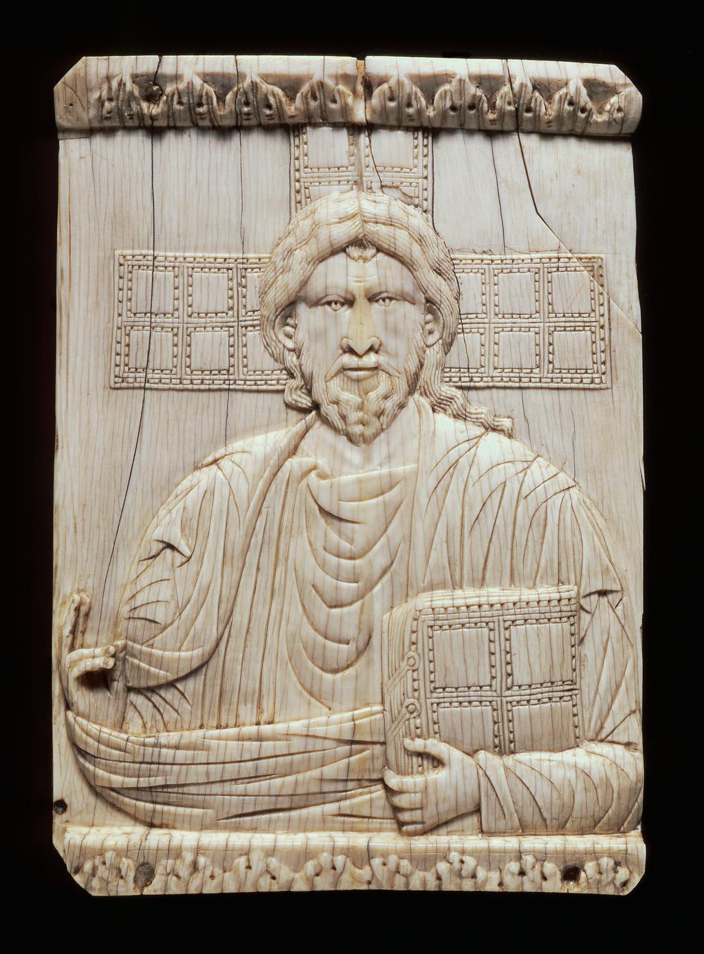An image of Sculpture/Panel. Christ Pantocrator represented half-length and full-face. Christ holds a book in his left hand and blesses with his right. Behind is seen the three upper limbs of the cross, the surfaces chequered in the same way as the book in Christ's hand. It is from the modern cover of a 10th century lectionary written at Reichenau. Height 138.0 mm, width 97.0 mm, circa 900 to 1000. Production Place: Byzantium.