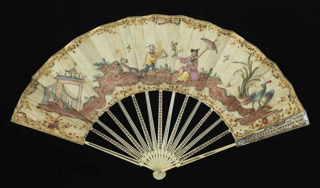 An image of Folding fan. Production Place: England and France. On the silk obverse is a chinoiserie figurative scene painted in gouache and gold paint and decorated with gilt-thread tambour-work outlining, stitched coloured-metal sequins (blue and yellow) and adhered coloured metal foil (red and blue) paillettes. The top edge and sides of the leaf are edged with applied gilt paper. Decoratively-carved sticks and guards of elephant ivory, overlaid with silver part-coloured by tinted lacquer; the ring-and dot motifs on the obverse sticks inlaid with red metal foil. Paper, previously silvered(?), is adhered to the reverse of alternate sticks. The sticks are united with a copper alloy rivet and mother-of-pearl spacers. Silk, backed with paper, length, guards, 27.5 cm, circa 1780. Chinoiserie.