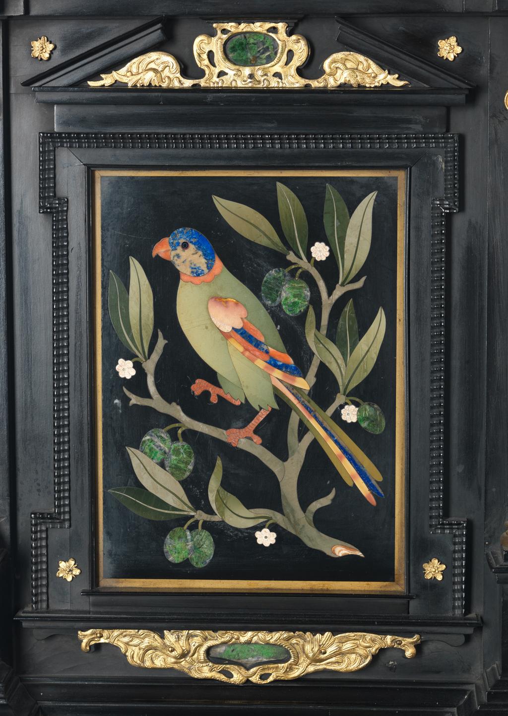 An image of Augsburg 17th century silver-gilt mounted ebony Table Cabinet with Florentine pietre dure plaques from the Grand Ducal workshops. Boscher, Elias (1600-1674). Of architectural form, the stepped superstructure fitted with three frieze drawers above a central cupboard door, architectural pediment and inset with a panel depicting a chaffinch on a fruiting bough, flanked by columns of Smaragdite Gabbro with Corinthian capitals flanked by two deep drawers, inset with panels depicting parrots within fruiting boughs, with three further fitted drawers below, the large central cupboard door inset with a panel of a lapis lazuli flower filled urn issuing stems including a carnation, anemone, daffodil and lilies and enclosing an architectural interior, flanked by further Smaragdite Gabbro Ionic columns and three drawers to each side inset with further symmetrical floral panels including tulips, roses, carnations, lilies and bluebells, on shaped bracket feet, each side inset with large central panels of parrots on fruiting boughs, with four further floral panels above and below, the reverse veneered in kingwood, amaranth and stained walnut in geometric stellar designs. The cabinet containing a complex series of fourty-four secret drawers and compartments to the interior. The cabinet is signed in pencil on the underside 'Elias Boscher' and 'gemacht'. The central cabochon mount stamped with the Augsburg town mark and the silversmiths mark of Johann Spitzmacher (active 1655-1678). The front bears the ebony stamp "EBEN" with the pinecone of Augsburg. Height 85 cm, width 84cm, depth 40cm, circa 1660.