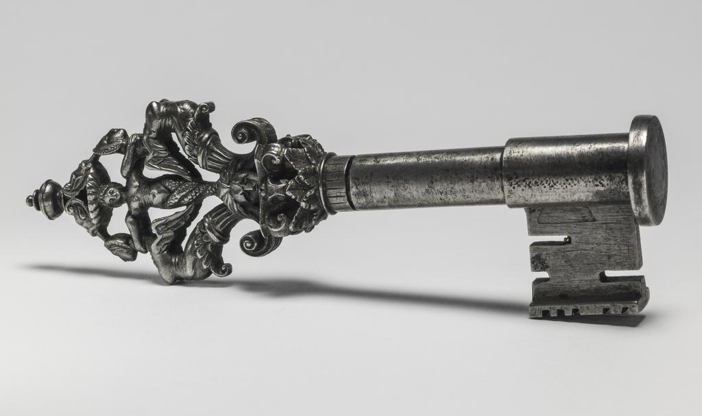 An image of Key. Iron, with piped stem, spade-shaped in section, collar in the form of a capital of Corinthian type and bow composed of two winged grotesque female figures back to back with a mermaid between them. Circa 1500-1600. French. Notes: Has cover for the stem.