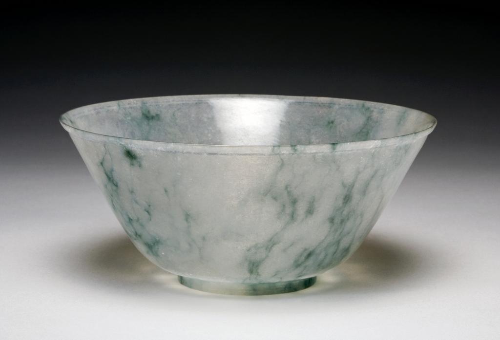 An image of Jadeite bowl of icy tone with dark green inclusions, rounded sides rising from a crisp foot to a flaring rim. Jadeite, height, 7.5 cm, diameter, 17.2 cm, 1700-1800. Chinese.
