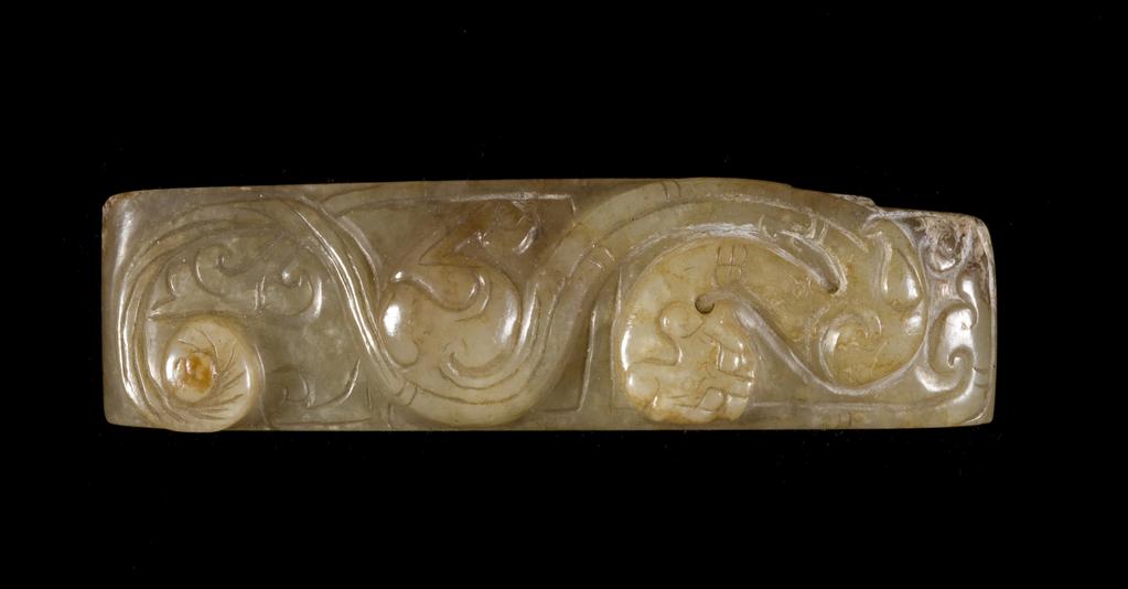 An image of Scabbard slide. Pale green translucent jade with some brown staining, decorated with a flattened version of a feline dragon. The underside of the piece is completely flat. Nephrite, height 1.25 cm, length 7.65 cm, width 1.9 cm, 1500-1700. Chinese.