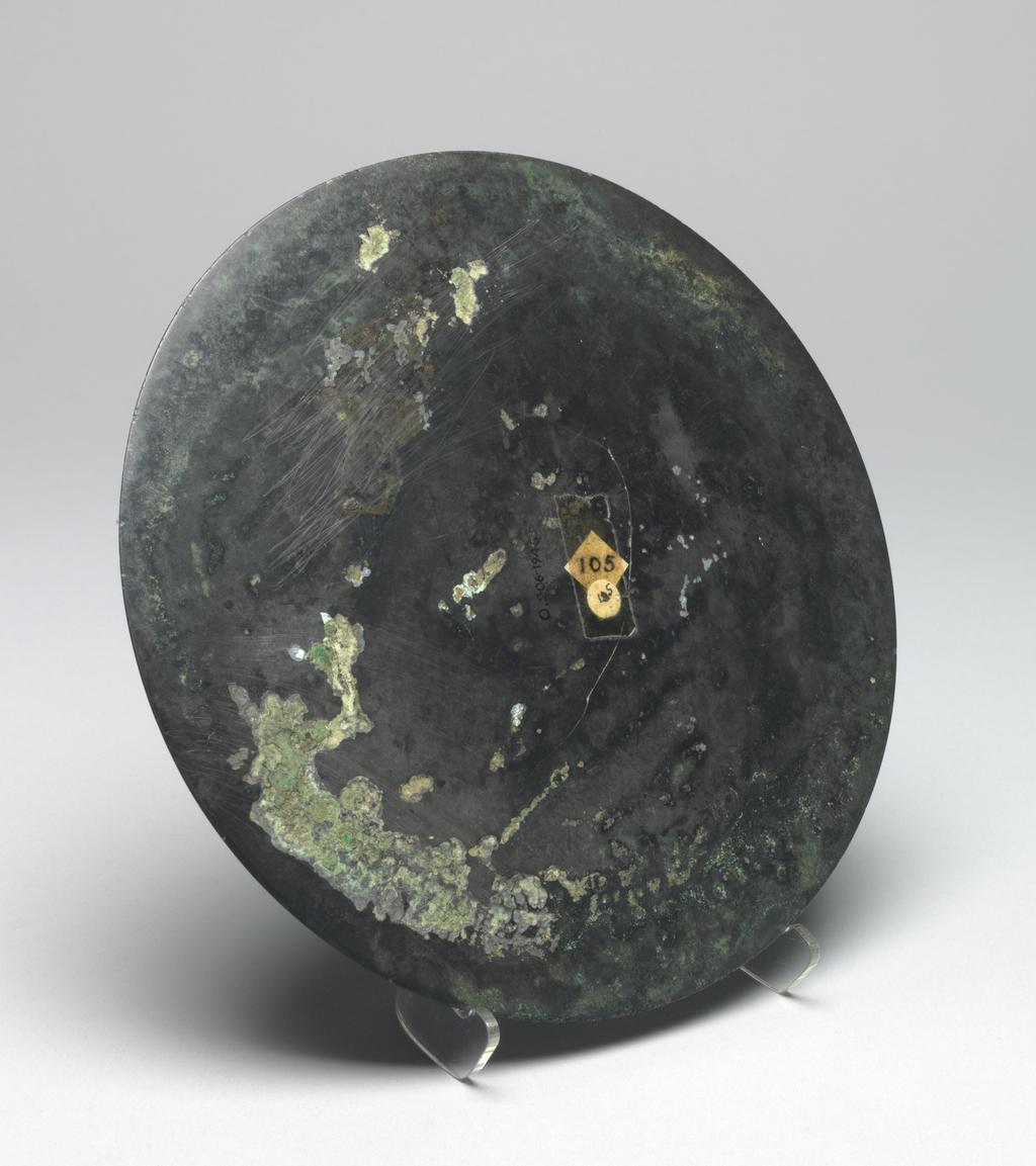 An image of Relief. Mirror made from bronze, inscribed with makers name (Teh'e). Around the central boss is a band of tail-less dragons, surmounted by a band of dragons, figures of men, and chariots. There is a band of inscription and a rim with dragons in light relief. Diameter 21.6 cm. Late Han Dynasty (206 BC-220 AD).