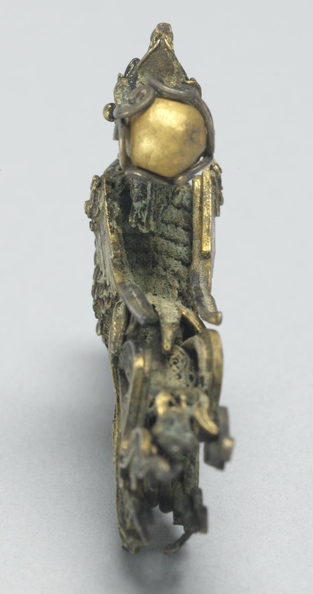 An image of Head of a hairpin. Hair ornament in gold filigree work. Unknown maker, China. It has the shape of a phoenix, which is standing on a cloud with extended tail feathers and with a raised head. The body and head of the phoenix are of thick plaited gold wires soldered together like feathers. The crest is in the form of a flower shaped receptacle for a gold bead. The phoenix is holding a bead in its beak. Beneath the cloud is a hole for fixing the bird to a head dress. Gold filigree, soldered, width 4.2 cm, height 3.8 cm. Tang Dynasty (618-907).