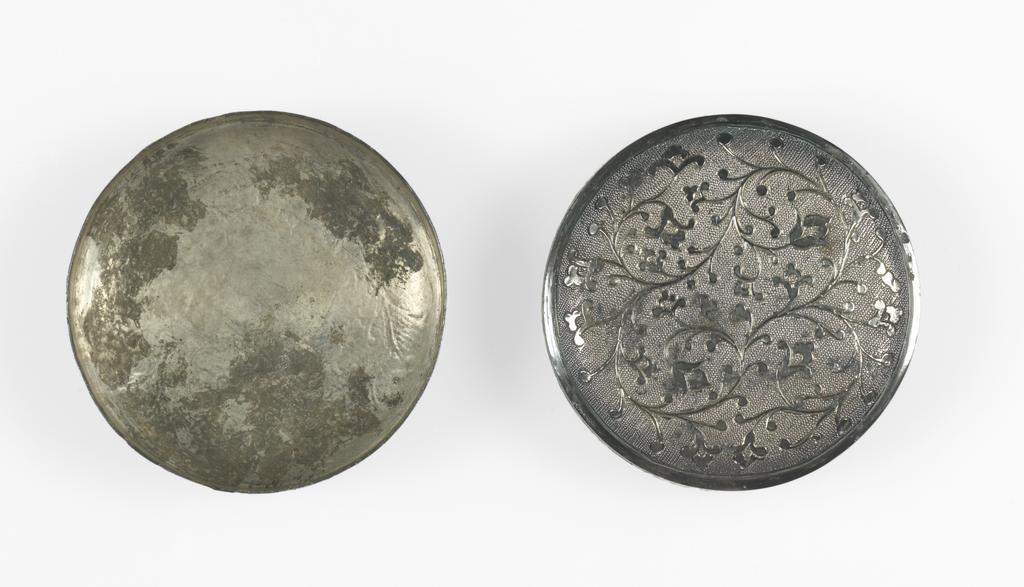 An image of Box. Unknown maker, China. Small circular box, made from beaten silver, of a slightly convex shape with straight sides. Both the box and the cover are decorated with foliate scrolls. The pattern has been gilded and is chased on a ground of regular ring matting. The sides have been soldered to the base. Silver, chased, gilded and engraved, diameter 5.2 cm, height 1.9 cm, T’ang Dynasty (618-906).