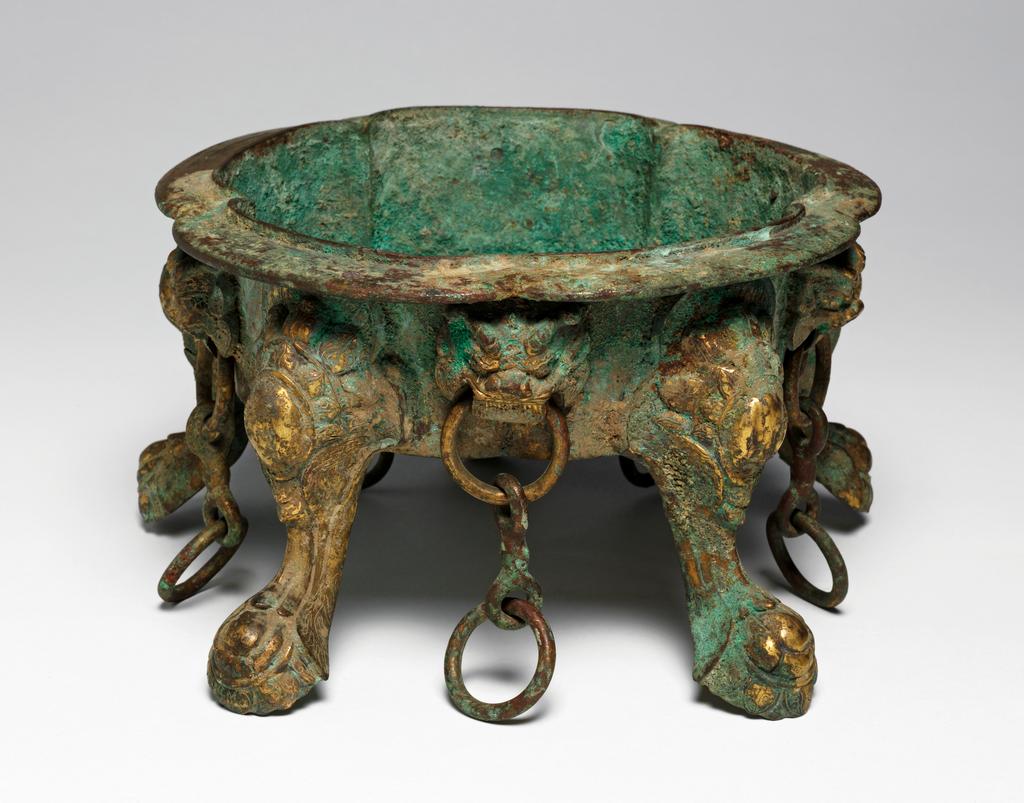 An image of Gilt-bronze censer, cast and supported on four cabriole legs, rising to an everted five-lobed rim, pierced through the sides with monster-face brackets suspending chains between each leg. Chinese, Tang dynasty. Circa 618 to 907 A.D.