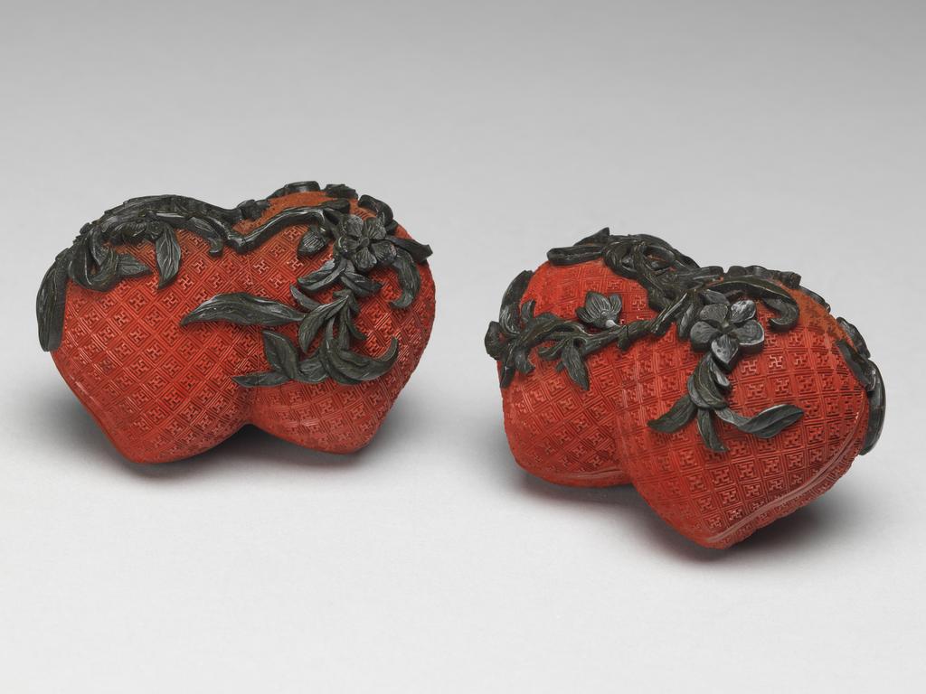 An image of A pair of small red lacquer boxes in the form of conjoined peaches, with stalks and blossoms in green lacquer, and gilding on the interior. Chinese.