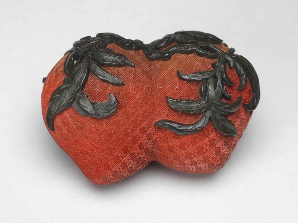 An image of A pair of small red lacquer boxes in the form of conjoined peaches, with stalks and blossoms in green lacquer, and gilding on the interior. Chinese.