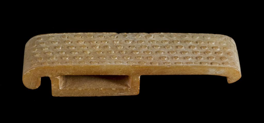 An image of Scabbard Slide. Brownish jade with some alterations on the surfaces, decorated with rows of small spirals in relief, enlivened by incised lines. Nephrite, height 1.6, cm, length 8.95 cm, width 2.3 cm, 1500-1700, Chinese.