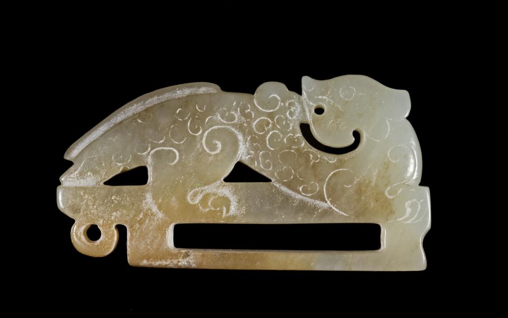 An image of Ornament. White tinged with green and brown jade, decorated with a dragon in the Han style. A hole on it suggests it was possibly a dress clasp. Nephrite, 1800-1900. Chinese.