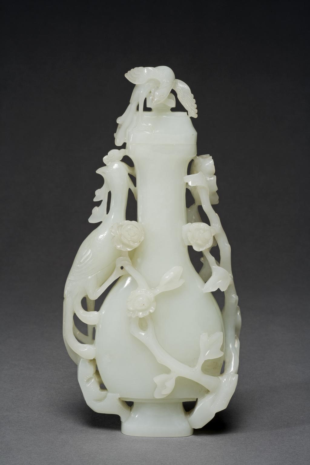 An image of White jade vase and cover, carved in high relief with a phoenix standing on top of a tree peony. The domed cover with a small phoenix standing on a square finial. Nephrite, height, with lid, 20.5, cm, width, 10, cm, 1800-1900. Chinese.