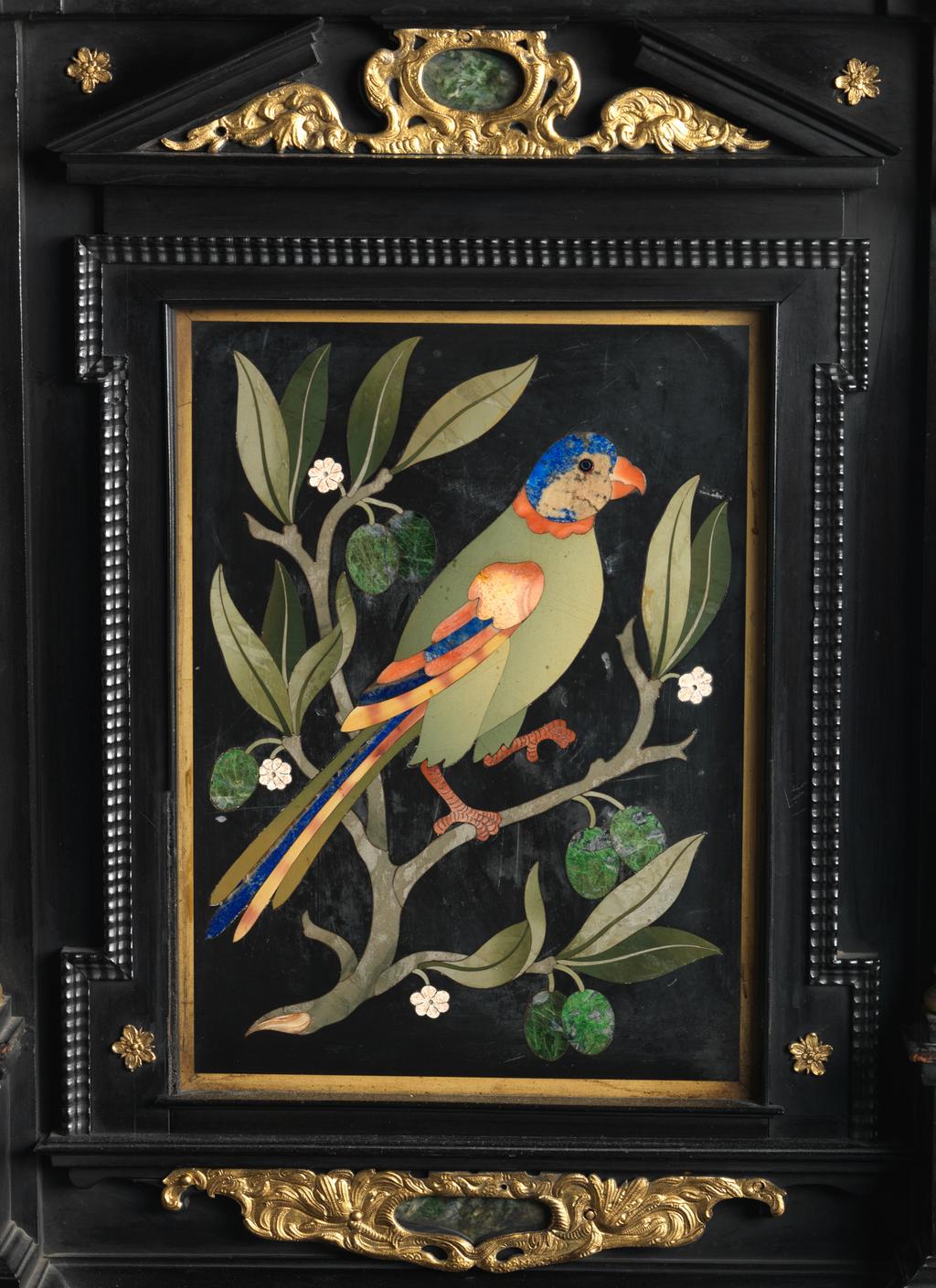 An image of Augsburg 17th century silver-gilt mounted ebony Table Cabinet with Florentine pietre dure plaques from the Grand Ducal workshops. Boscher, Elias (1600-1674). Of architectural form, the stepped superstructure fitted with three frieze drawers above a central cupboard door, architectural pediment and inset with a panel depicting a chaffinch on a fruiting bough, flanked by columns of Smaragdite Gabbro with Corinthian capitals flanked by two deep drawers, inset with panels depicting parrots within fruiting boughs, with three further fitted drawers below, the large central cupboard door inset with a panel of a lapis lazuli flower filled urn issuing stems including a carnation, anemone, daffodil and lilies and enclosing an architectural interior, flanked by further Smaragdite Gabbro Ionic columns and three drawers to each side inset with further symmetrical floral panels including tulips, roses, carnations, lilies and bluebells, on shaped bracket feet, each side inset with large central panels of parrots on fruiting boughs, with four further floral panels above and below, the reverse veneered in kingwood, amaranth and stained walnut in geometric stellar designs. The cabinet containing a complex series of fourty-four secret drawers and compartments to the interior. The cabinet is signed in pencil on the underside 'Elias Boscher' and 'gemacht'. The central cabochon mount stamped with the Augsburg town mark and the silversmiths mark of Johann Spitzmacher (active 1655-1678). The front bears the ebony stamp "EBEN" with the pinecone of Augsburg. Height 85 cm, width 84cm, depth 40cm, circa 1660.