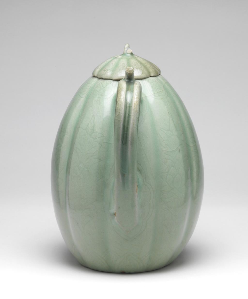An image of Melon-shaped ewer and cover. Unknown pottery, possibly North Cholla province, Puan-gun, Yuch'on-ri kilns or South Cholla province, Kangjin-gun, Sadang-ri kilns. This ewer is melon-shaped, with ten lobes and a curved spout and handle, and has a flower-shaped lid with a lug for attachment to a lug at the handle. The footring is very low. A band of petal panels is incised around the top and one of lotus petals around the base of the ewer, and a spray of lotus with a fully opened bloom on each lobe. The lid has scrollwork incised on each lobe and the front of the spout a large single lotus leaf. The glaze is of a light bluish-green jade colour, evenly applied over the body; the lid is of a slightly different hue and may have been fired separately. There are five quartzite spur-marks on the base. Stoneware, thrown, with parts attached, indented, incised and celadon-glazed, height, whole, 22.2 cm, diameter, rim, 3.7 cm, diameter, foot, 9.0 cm, circa 1150-1200. Koryo Dynasty. Korea.